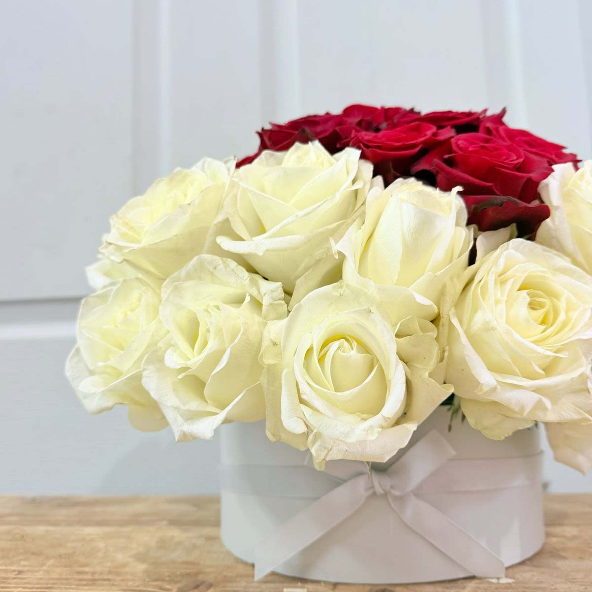 Red and white roses arranged in a white hat box with ribbon