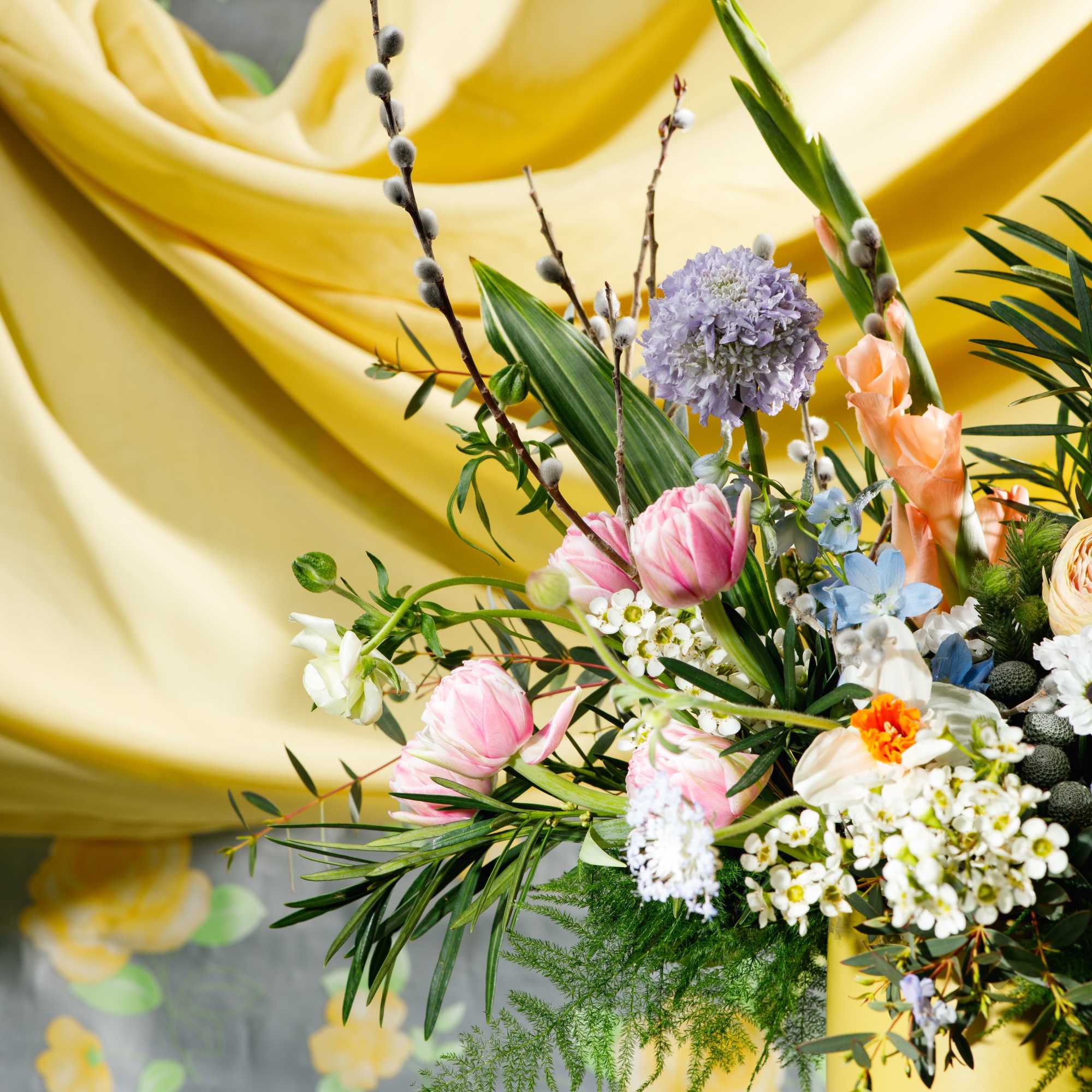 Pastel arrangement of pink tulips and mixed spring flowers in a yellow ceramic vase