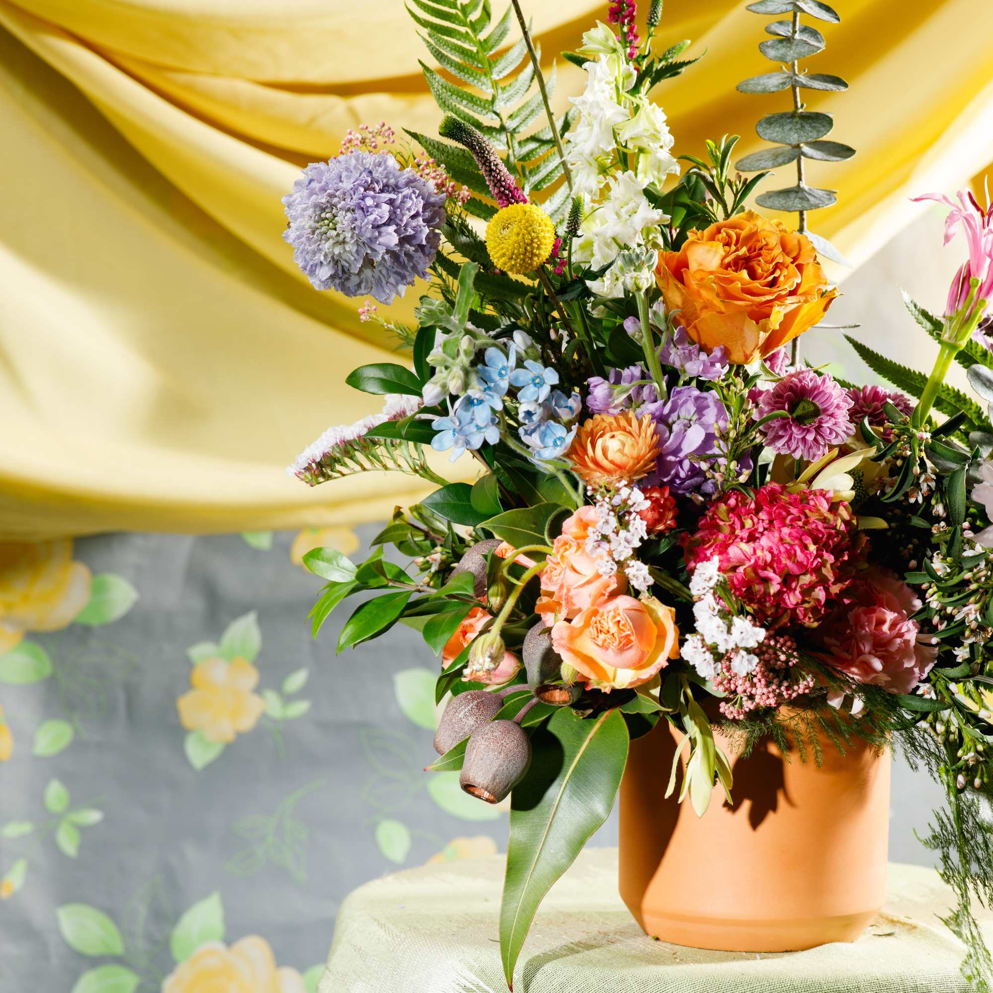 Colorful mixed flower arrangement with roses, hydrangea, and fern accents in a terracotta pot.