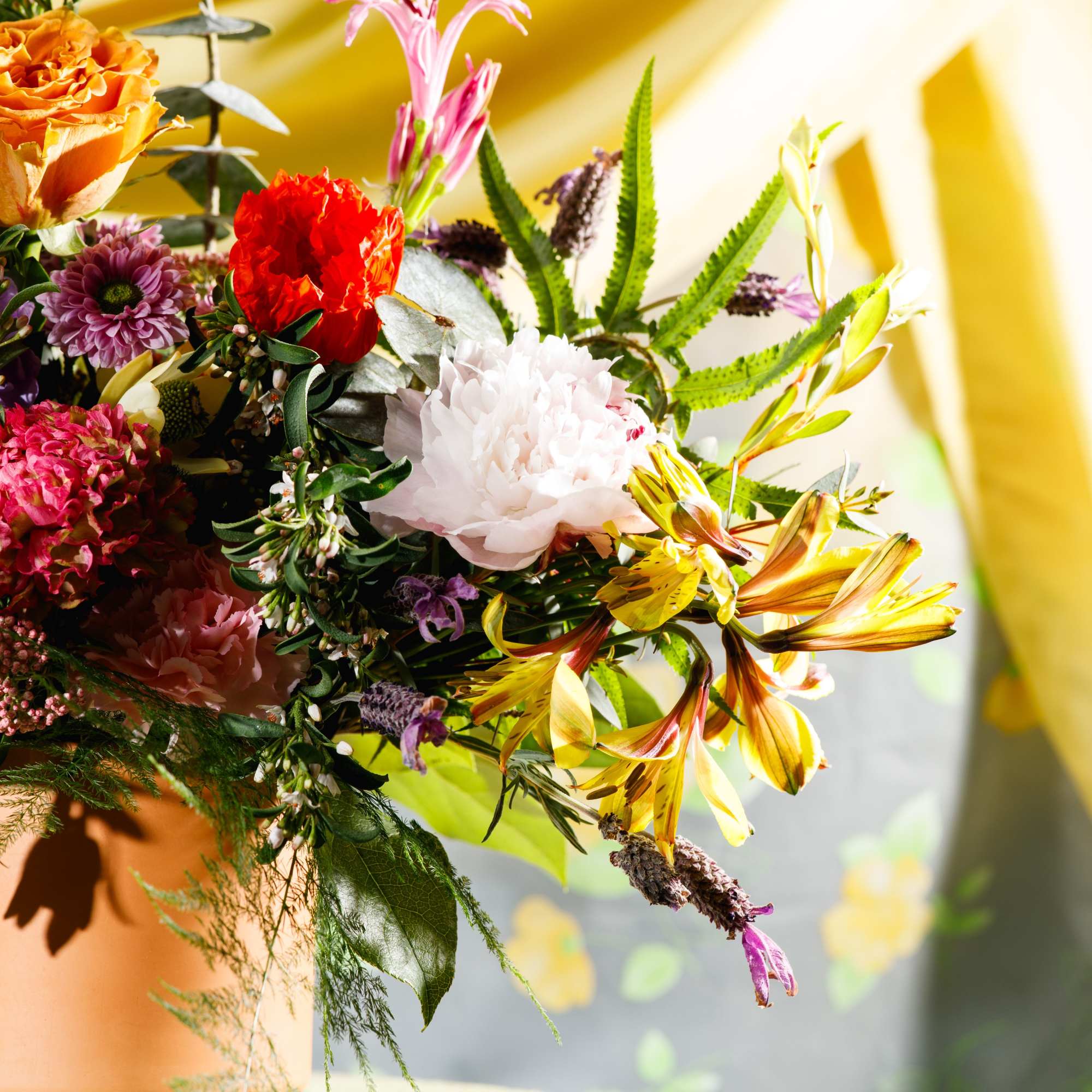 Colorful arrangement of yellow lilies and mixed pink and orange blooms in a terracotta pot on a draped table