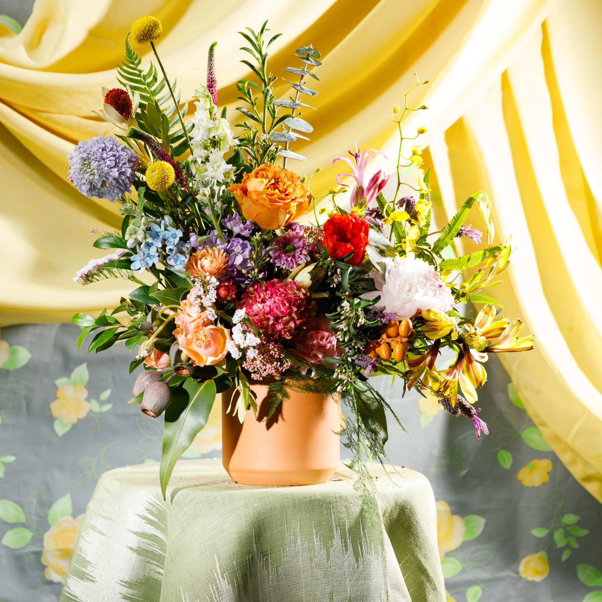 Colorful mixed flower arrangement in a terracotta pot on a draped table