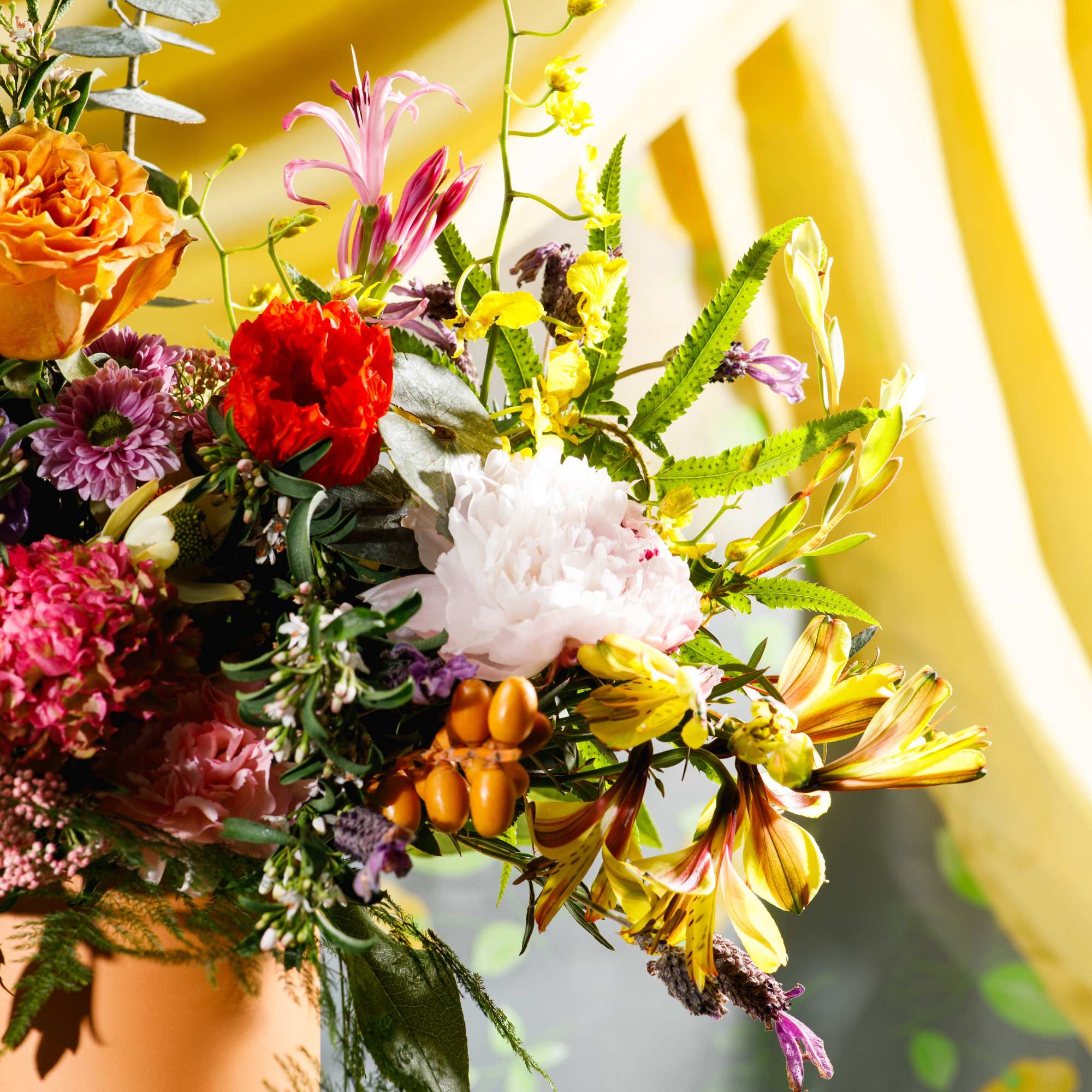 Lush mixed arrangement of yellow lilies, orange rose, red carnation, and white peony in a terracotta pot