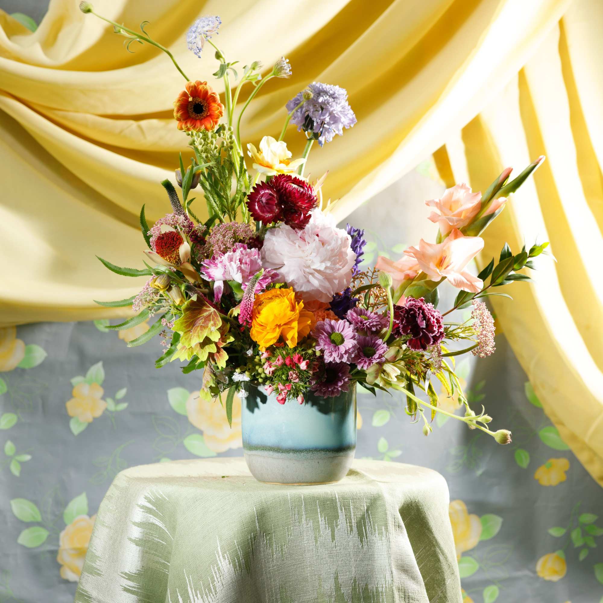 Colorful mixed flower arrangement in a blue ceramic vase on a draped table