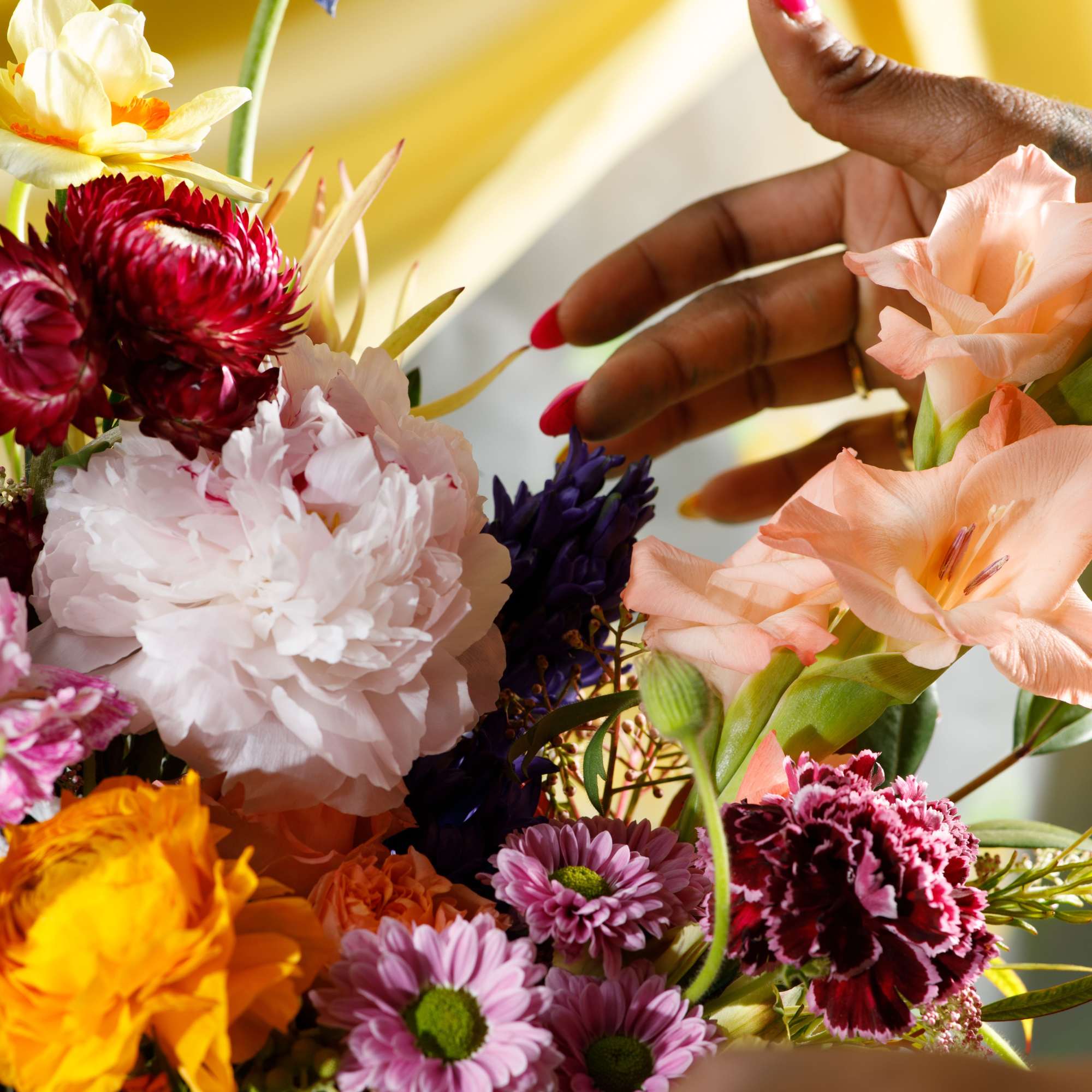 Colorful mixed bouquet with pink, peach, yellow and purple blooms being arranged by a hand.