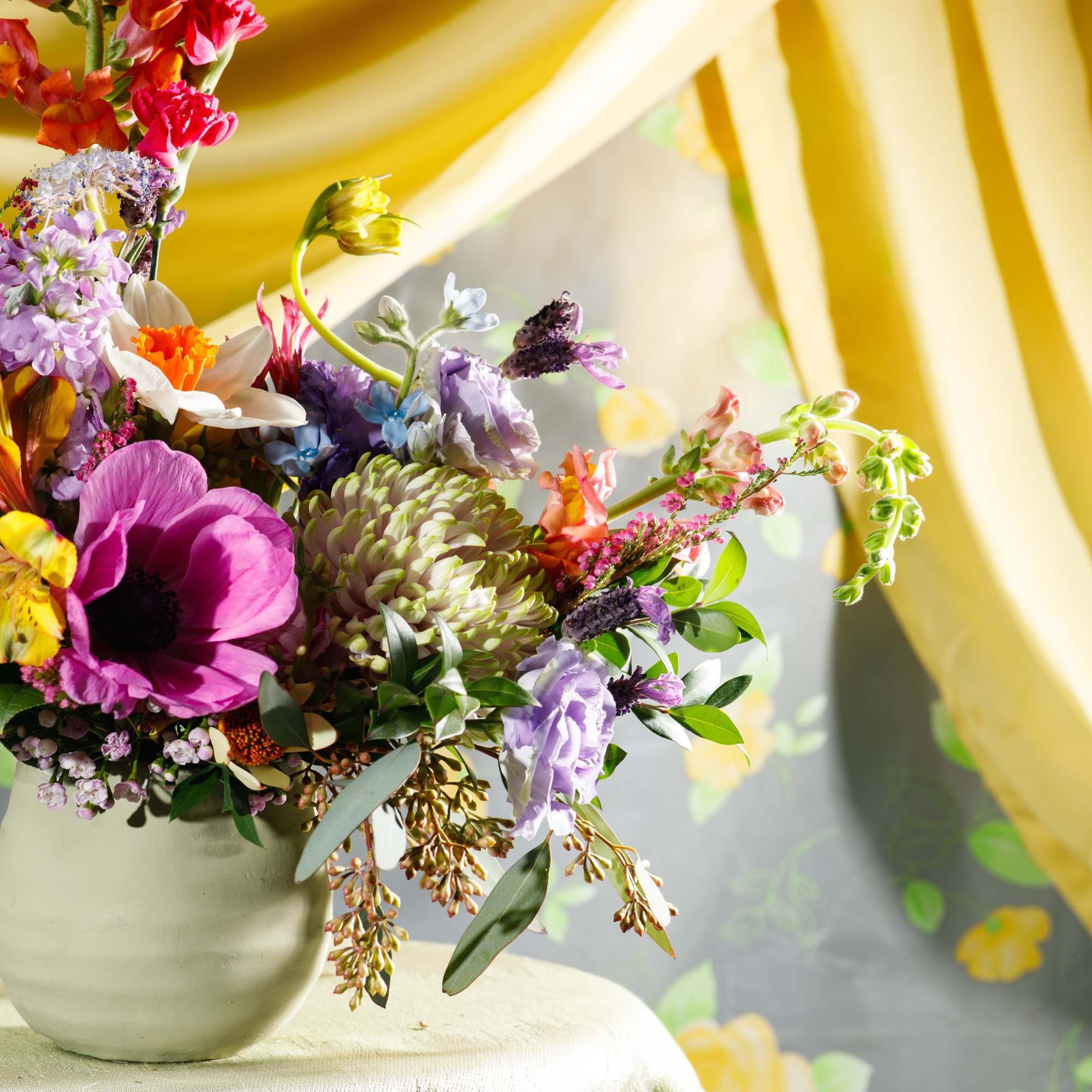 Colorful mixed flower arrangement in a pale green ceramic pot on a draped table