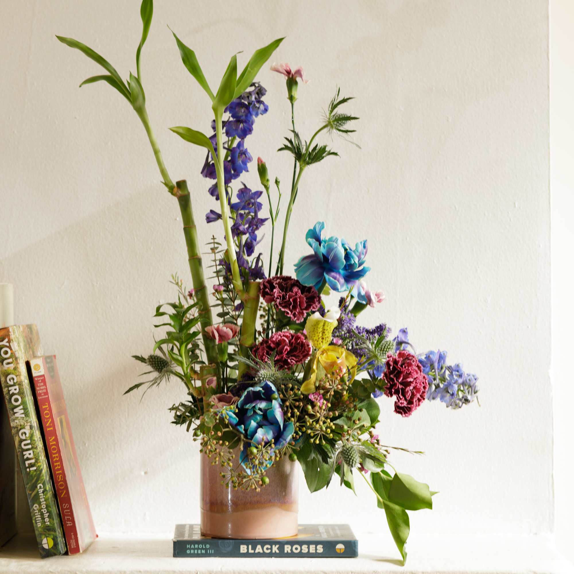 Tall mixed arrangement with blue, pink, and yellow blooms in a ceramic vase on a mantel.