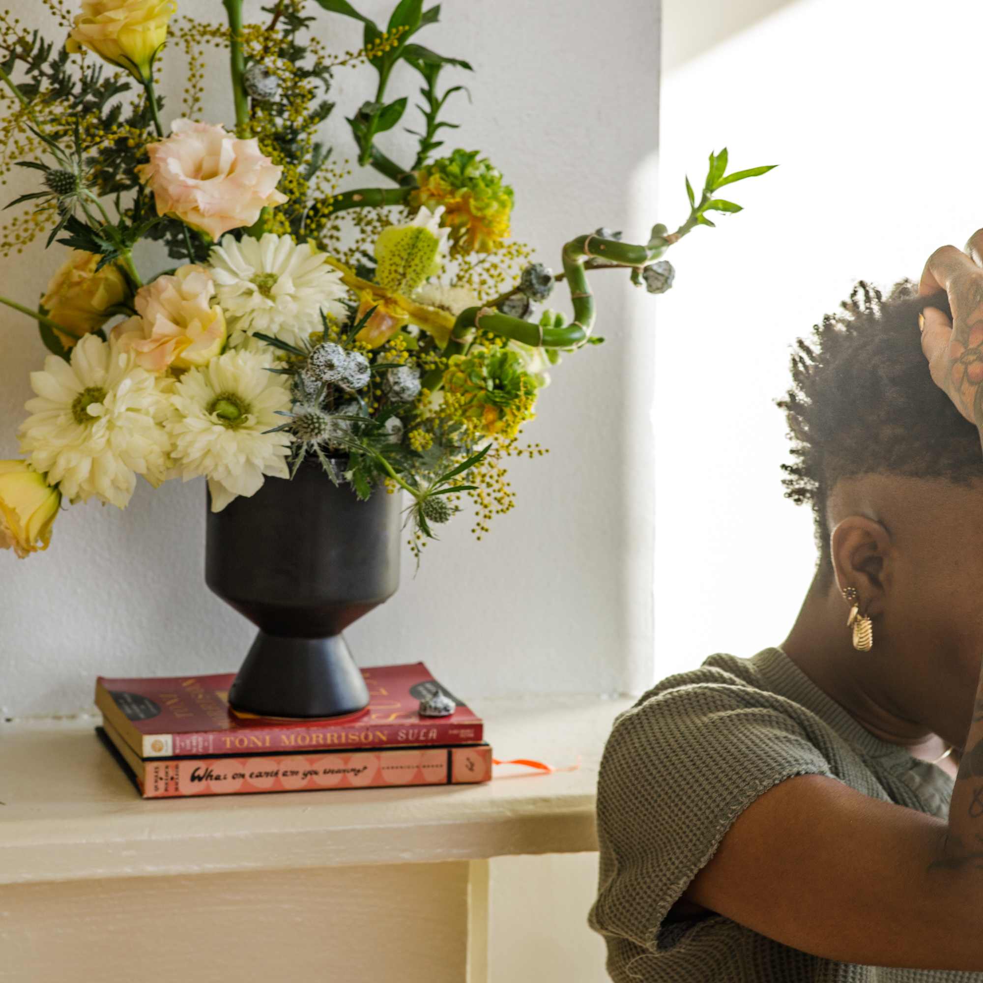 Mixed bouquet in a dark vase on stacked books beside a person