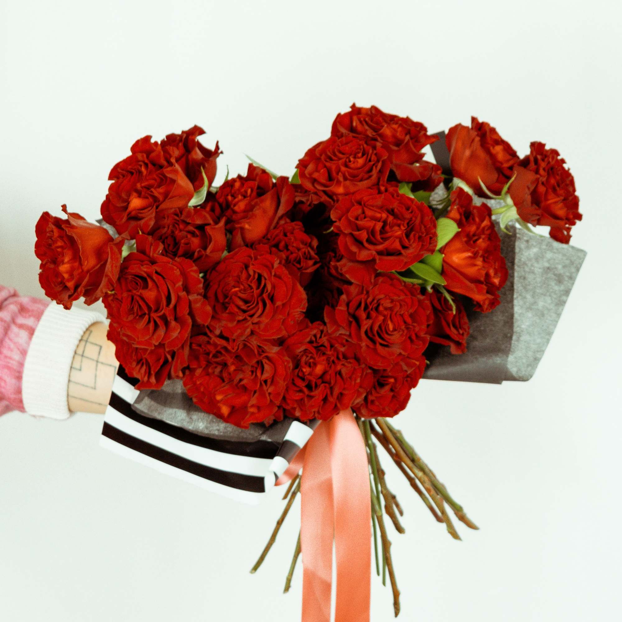 Bouquet of red roses wrapped in dark paper with a pink ribbon