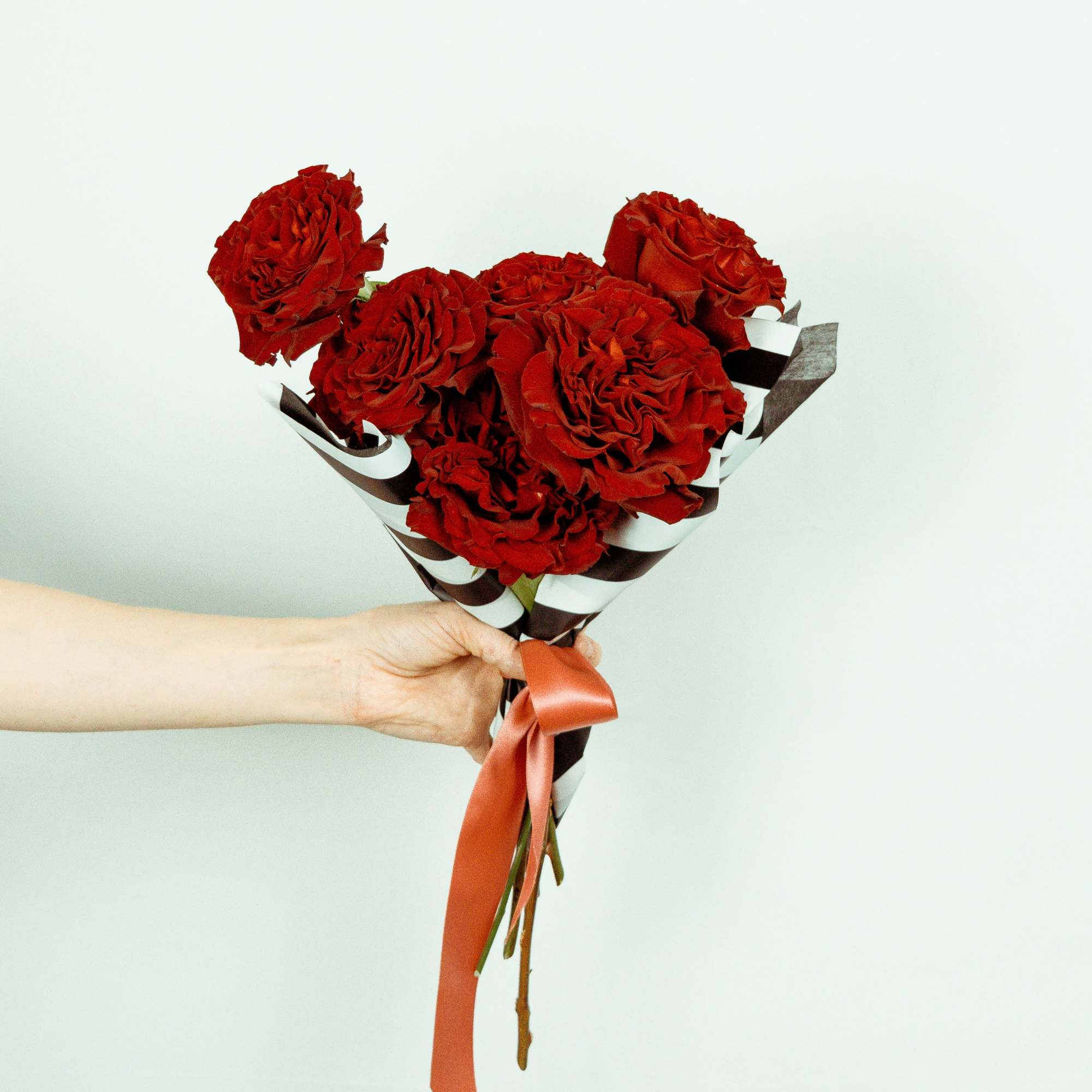 Handheld bouquet of red roses wrapped in striped paper with a ribbon