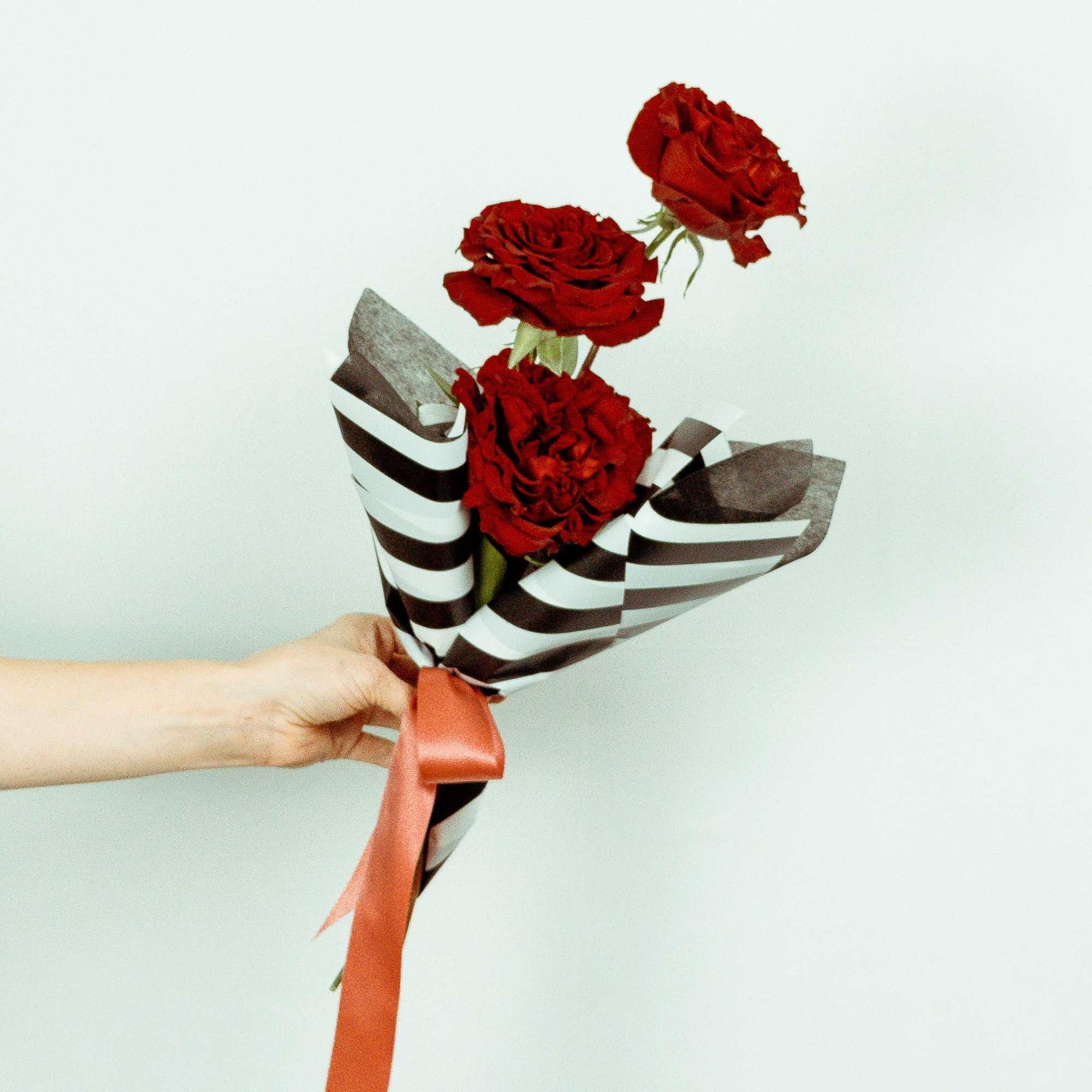 Three red roses wrapped in striped paper with a ribbon