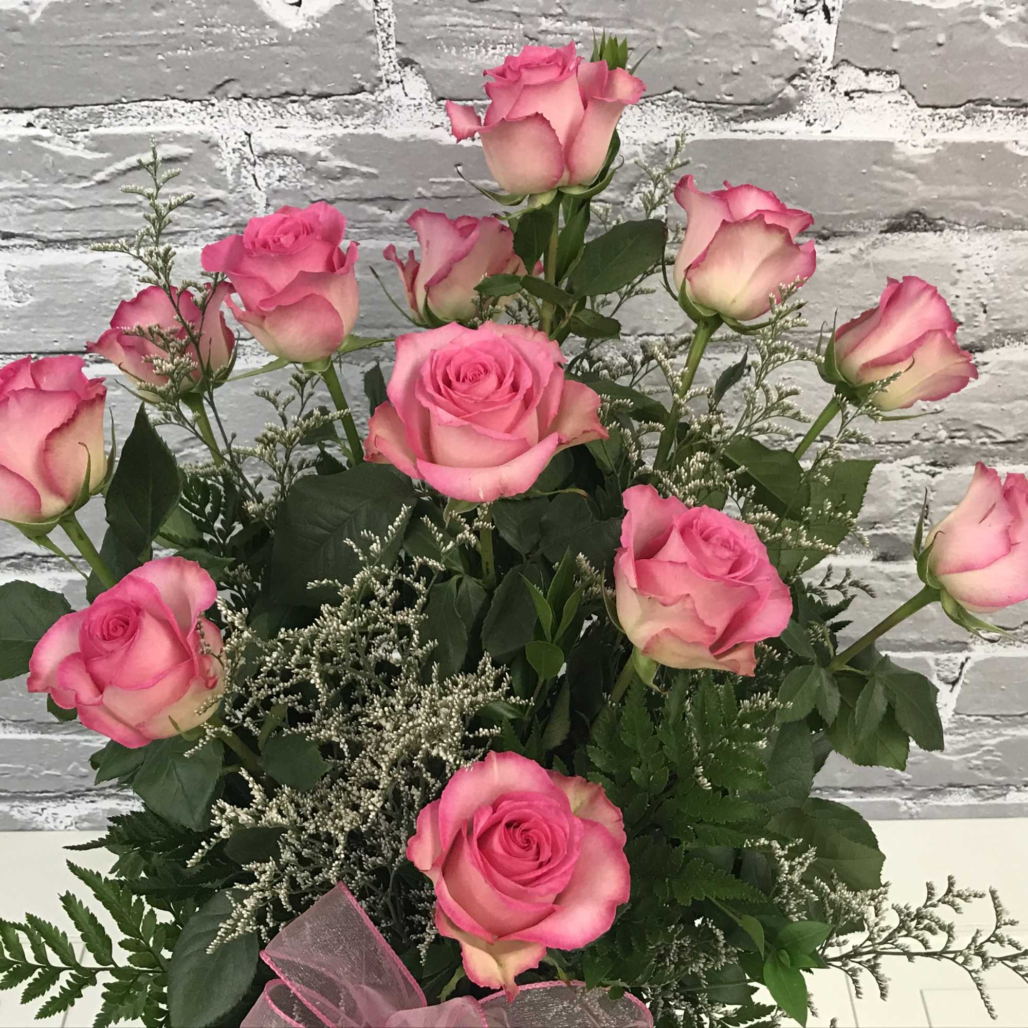 Pink roses arranged with greenery and a pink ribbon