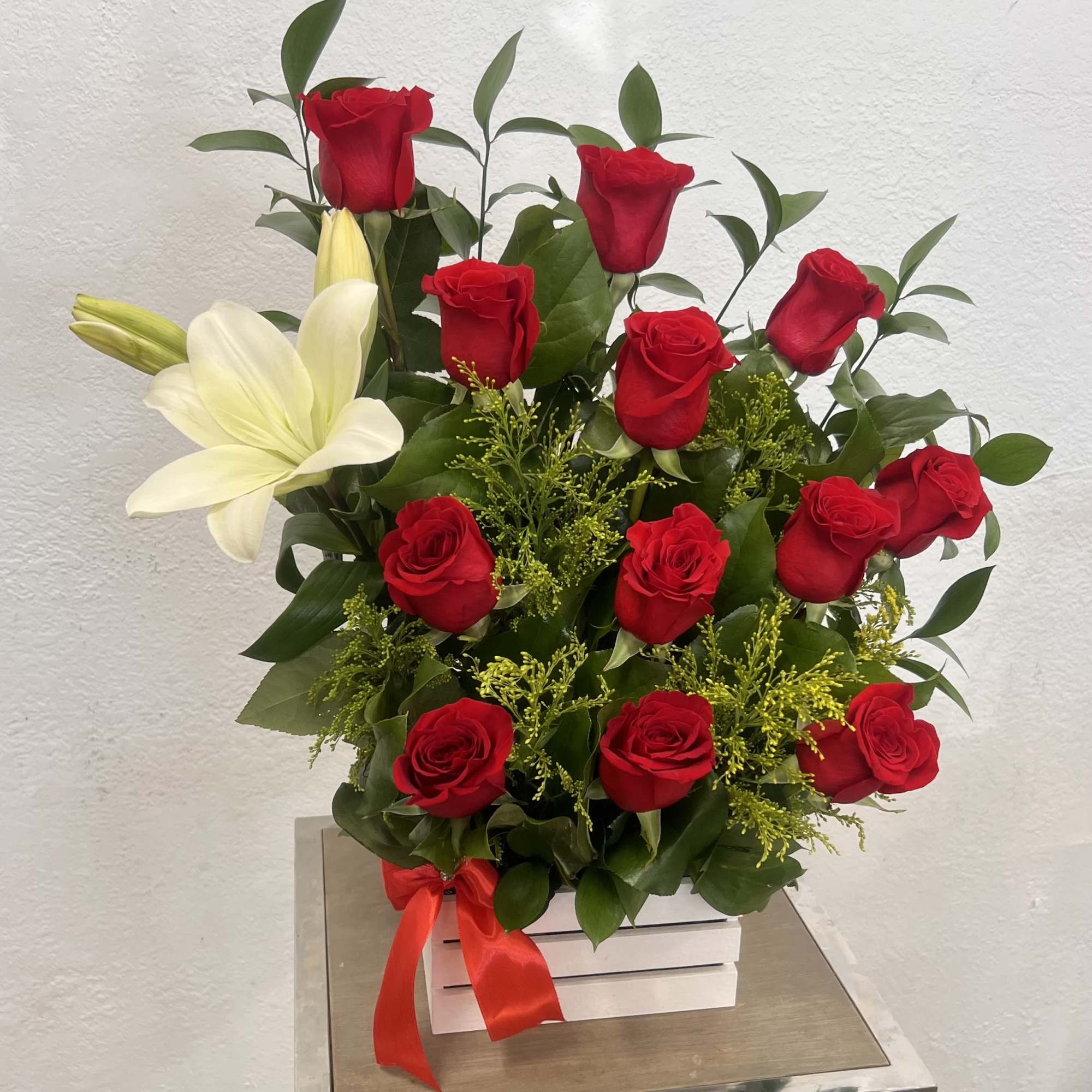 Red roses and a white lily in a white box with a red ribbon