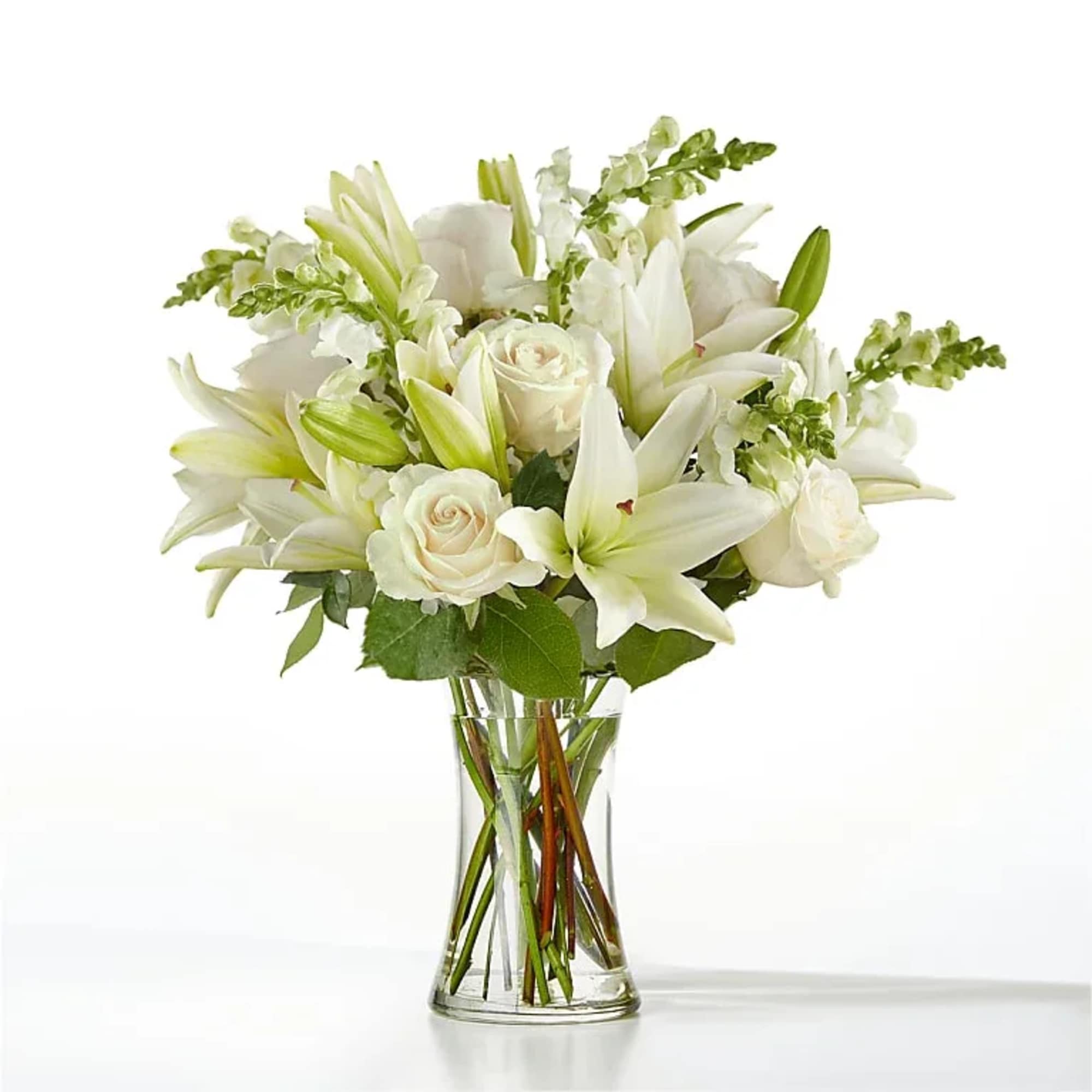 Arrangement of white lilies, roses, and snapdragons in a clear glass vase