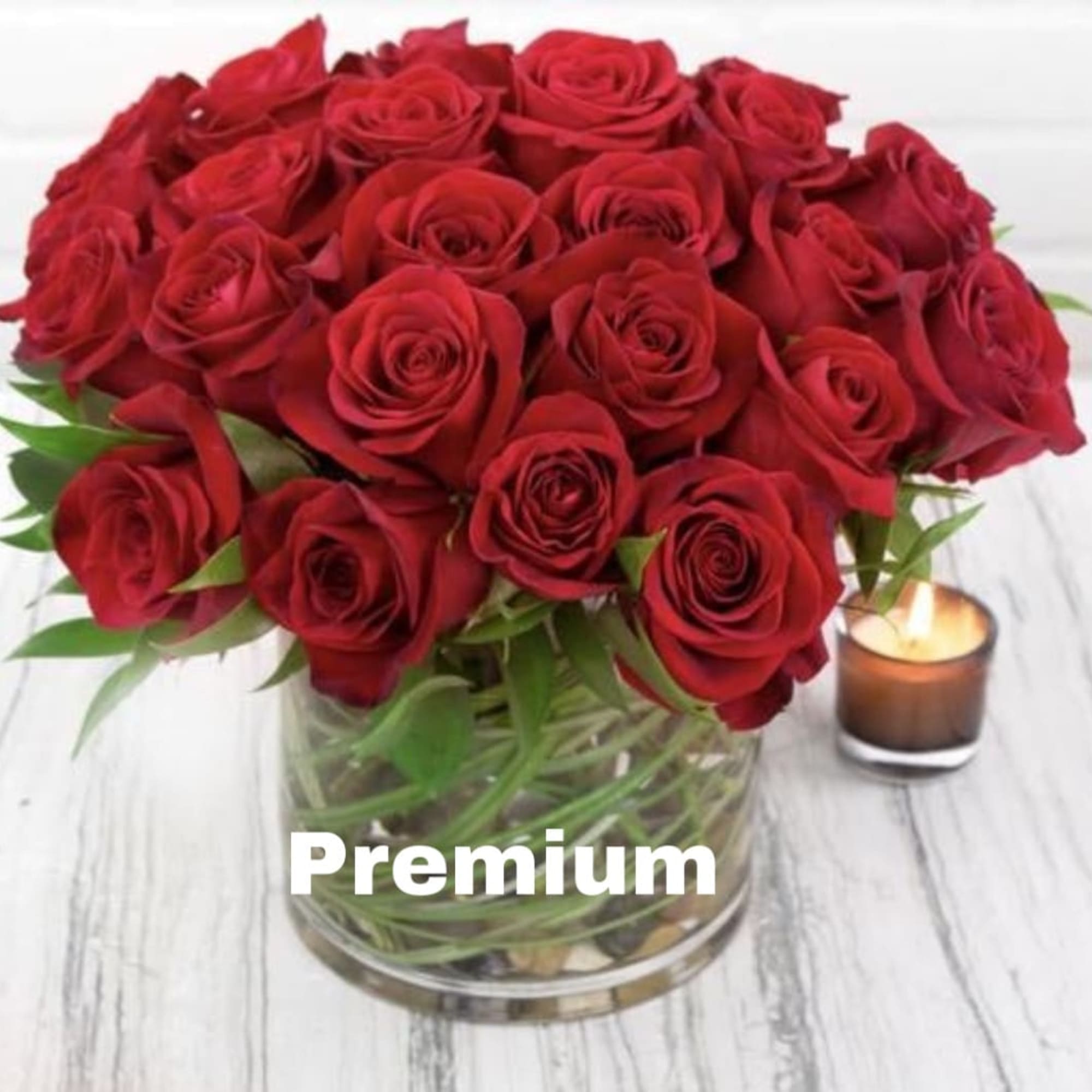 Red roses arranged in a clear glass vase beside a small candle