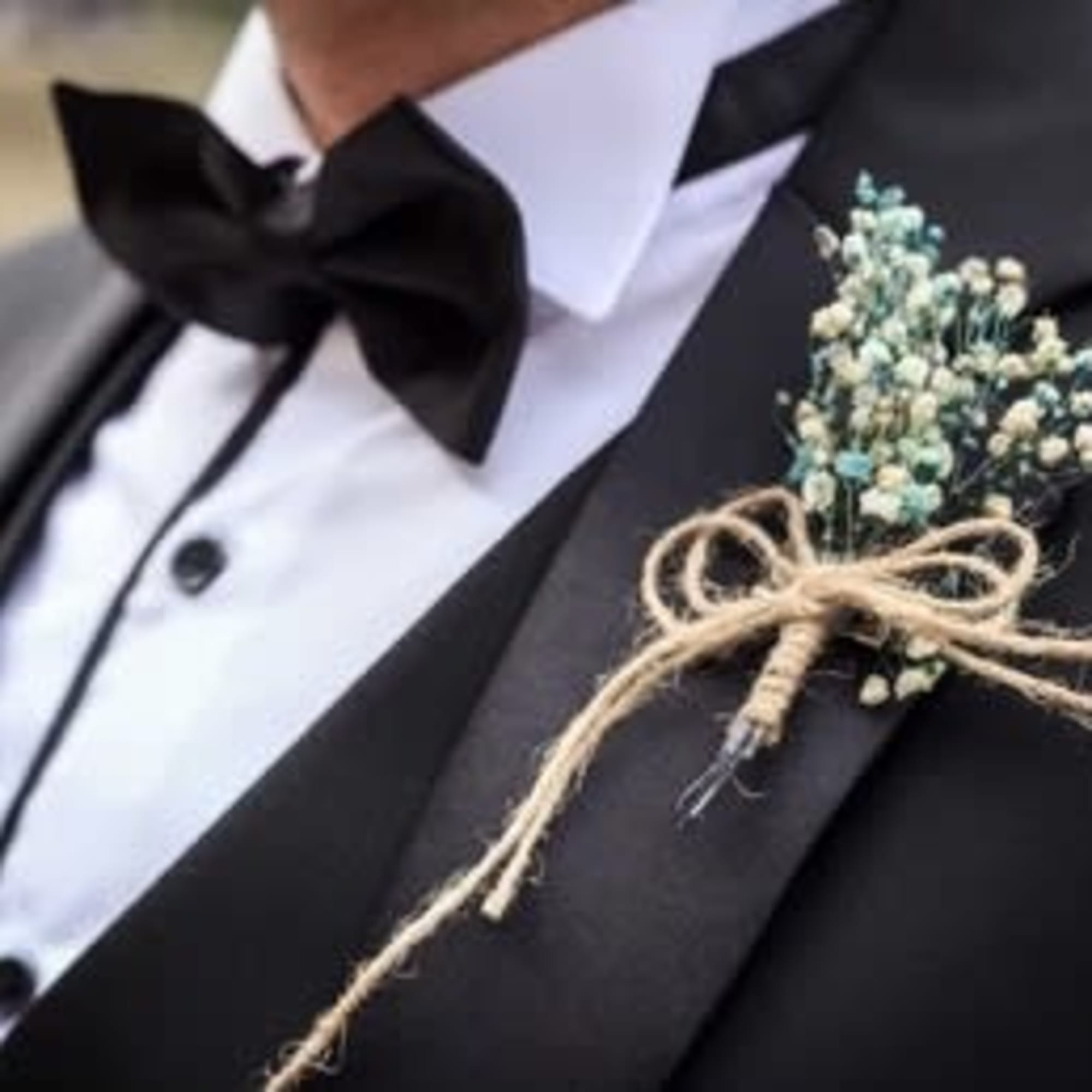 Boutonniere with tiny blue-white flowers tied to a black tuxedo lapel