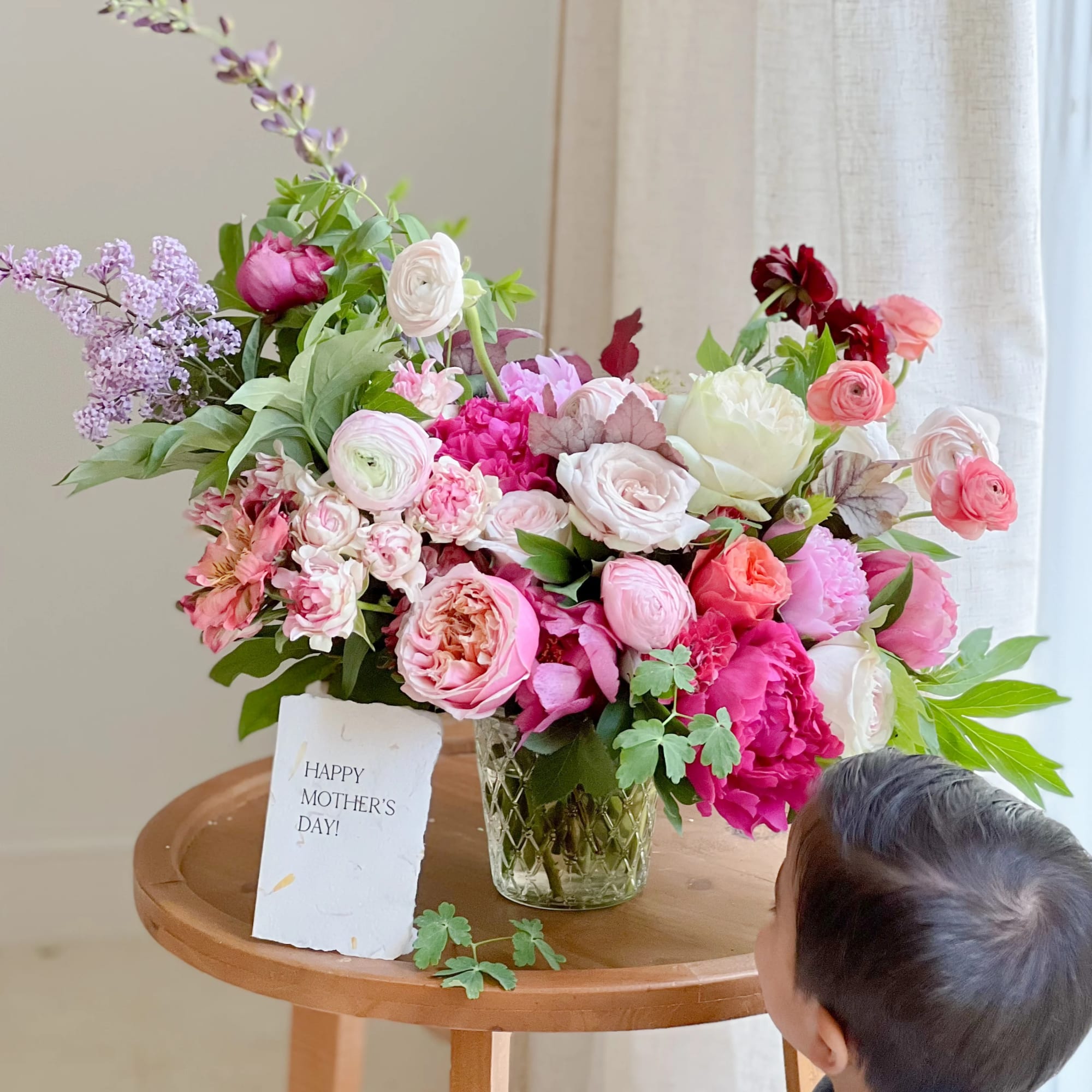 Mixed pink and white flower arrangement in a glass vase with a Mother's Day card