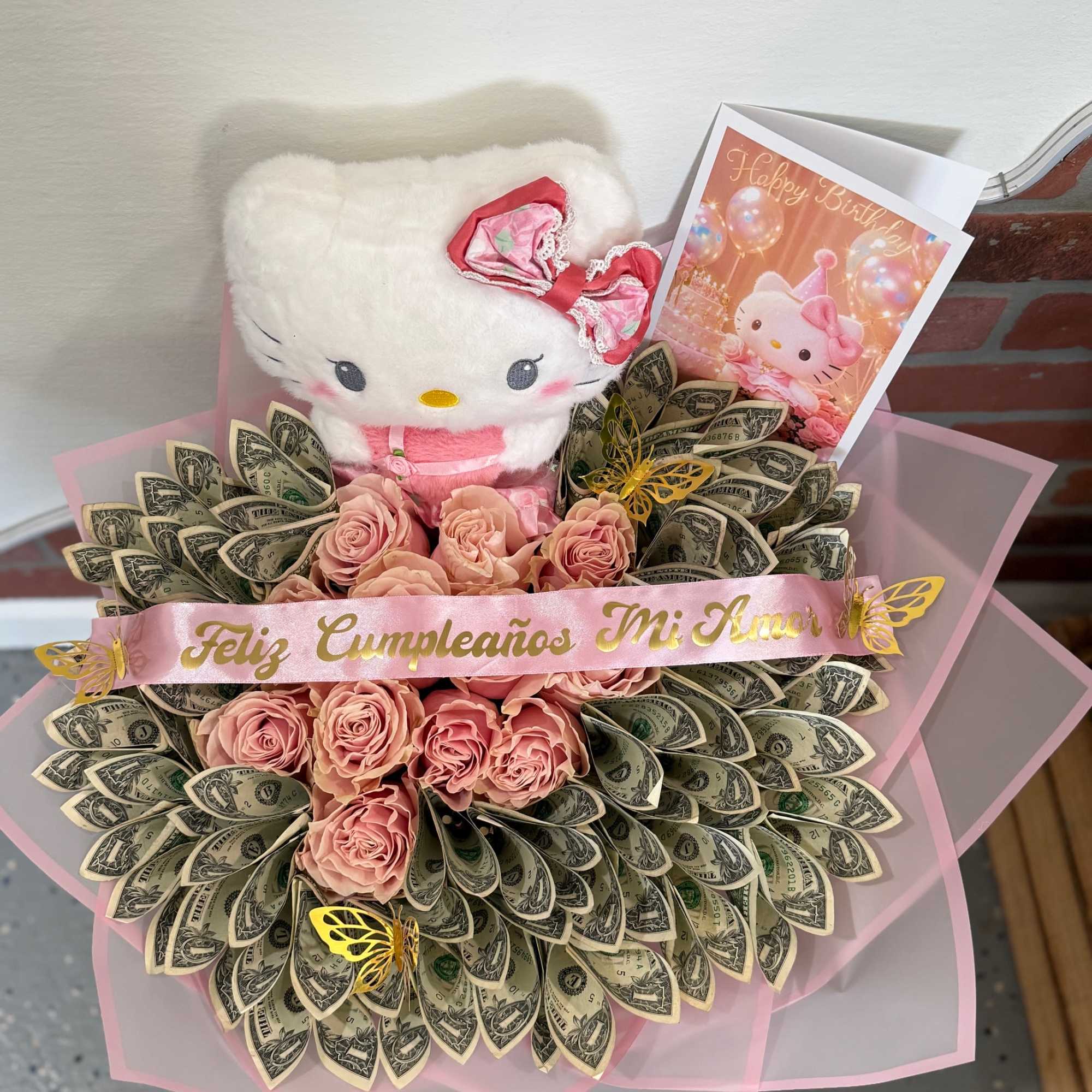 Hello Kitty plush with pink roses, dollar bills, and a birthday card