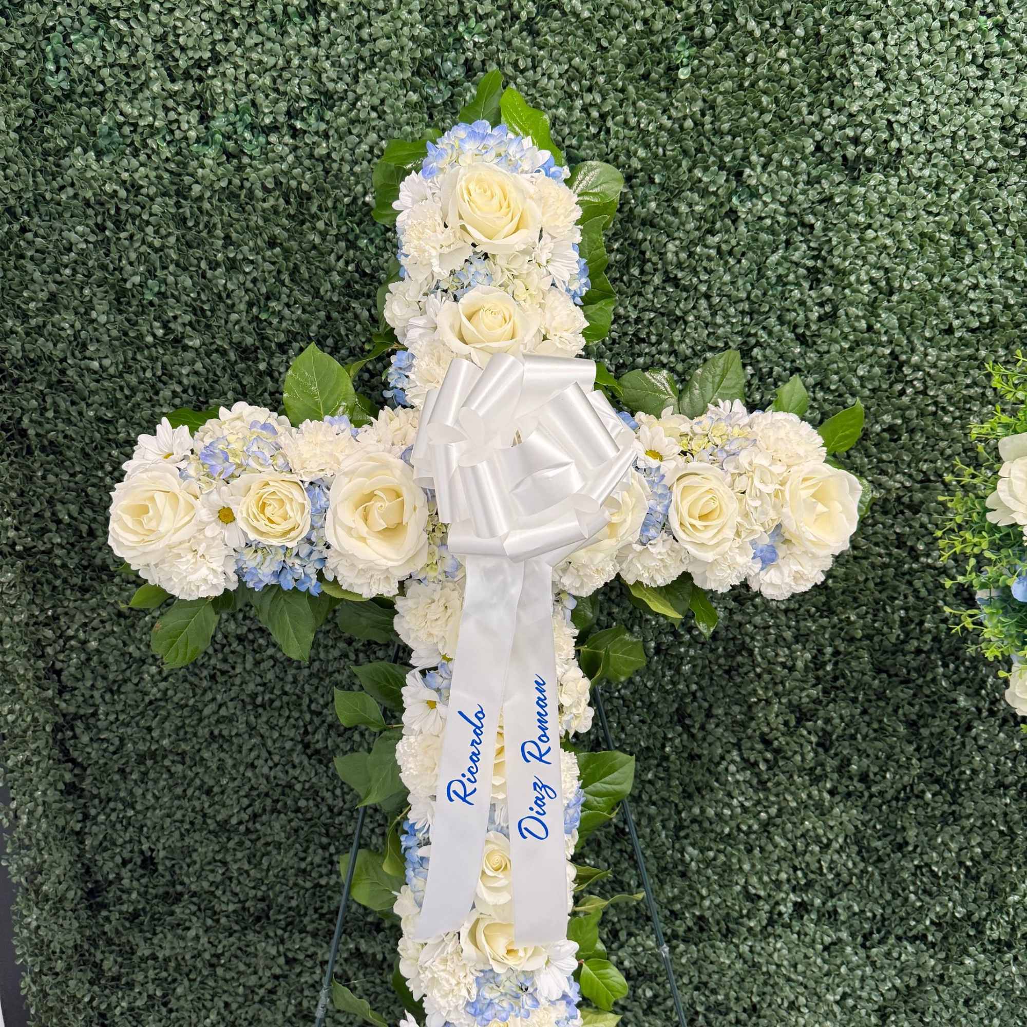 White floral cross with roses and blue accents on an easel