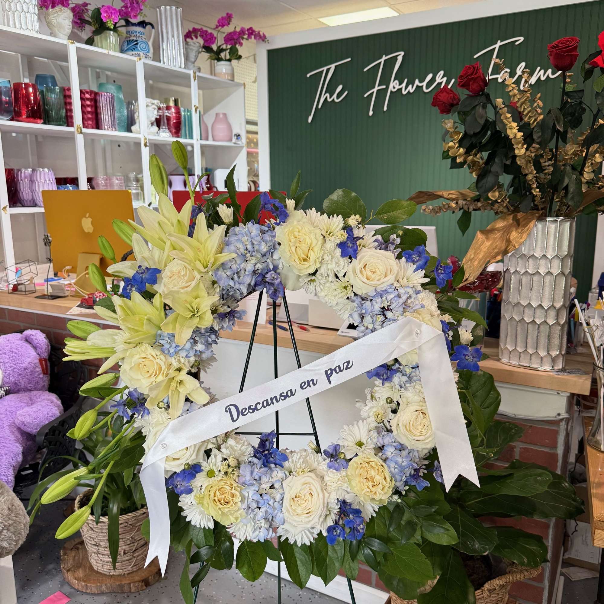Large funeral wreath of white, blue, and cream flowers on an easel with a ribbon