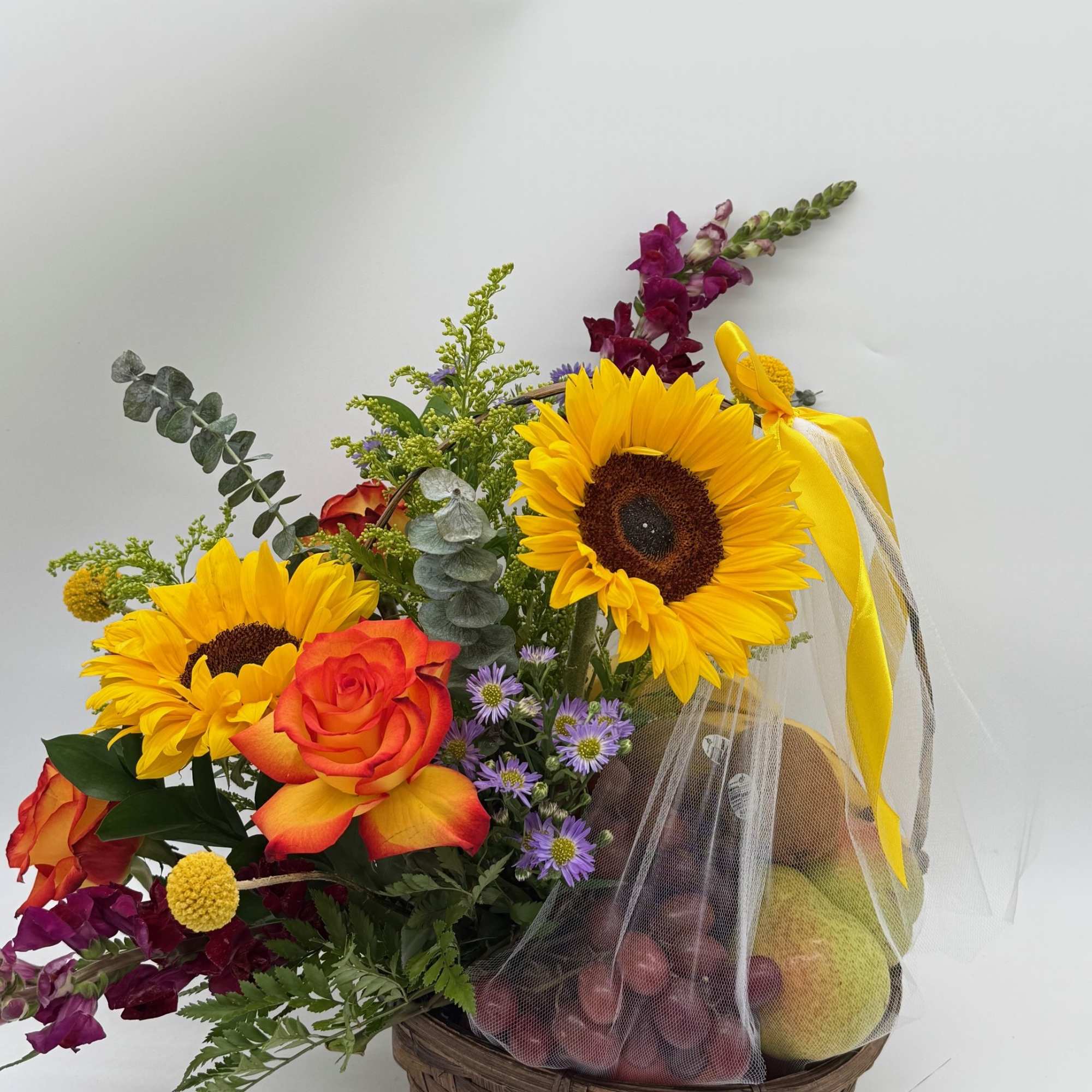 Basket arrangement with sunflowers, roses, and fruit in mesh wrap