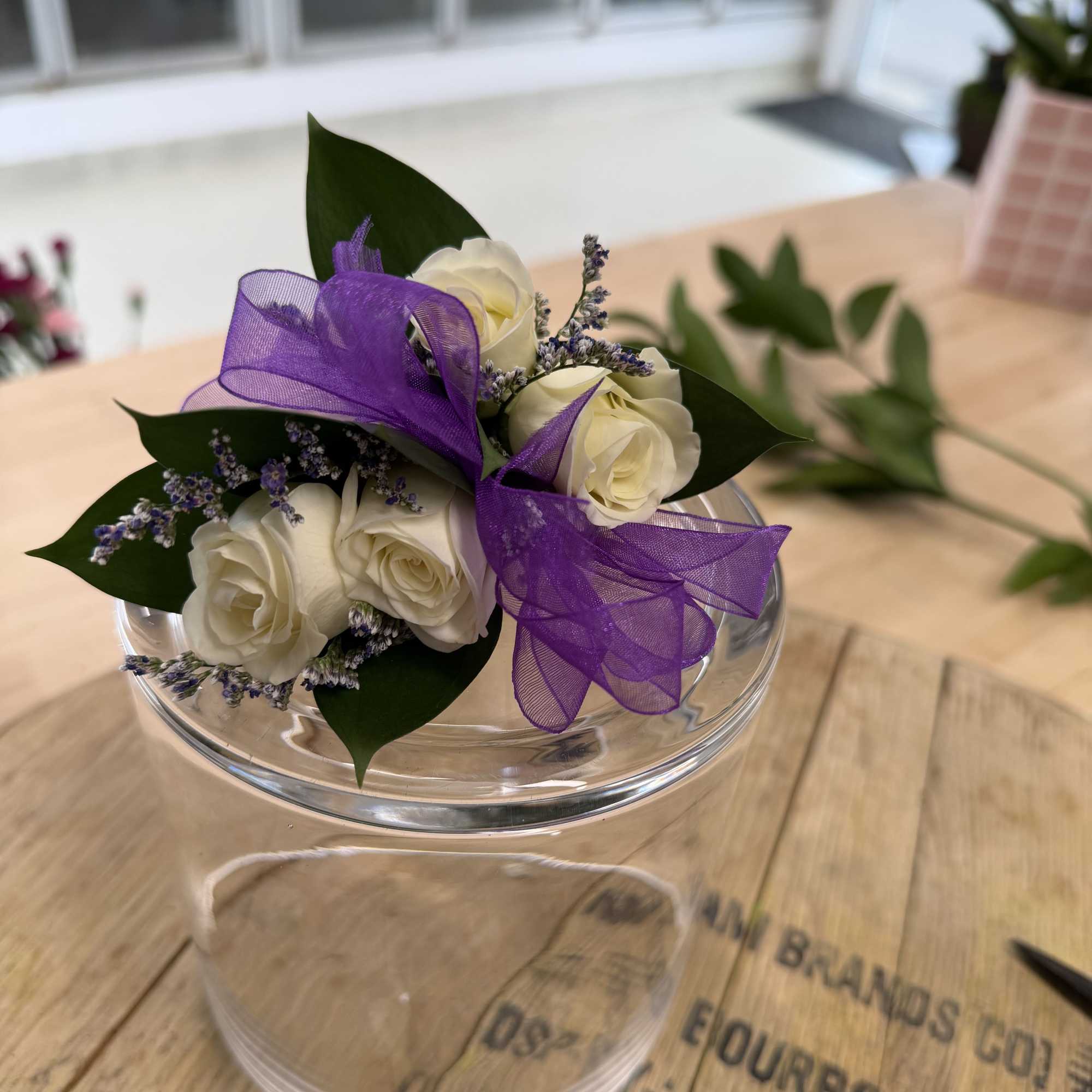 Small bouquet of white roses with a purple ribbon in a clear bowl