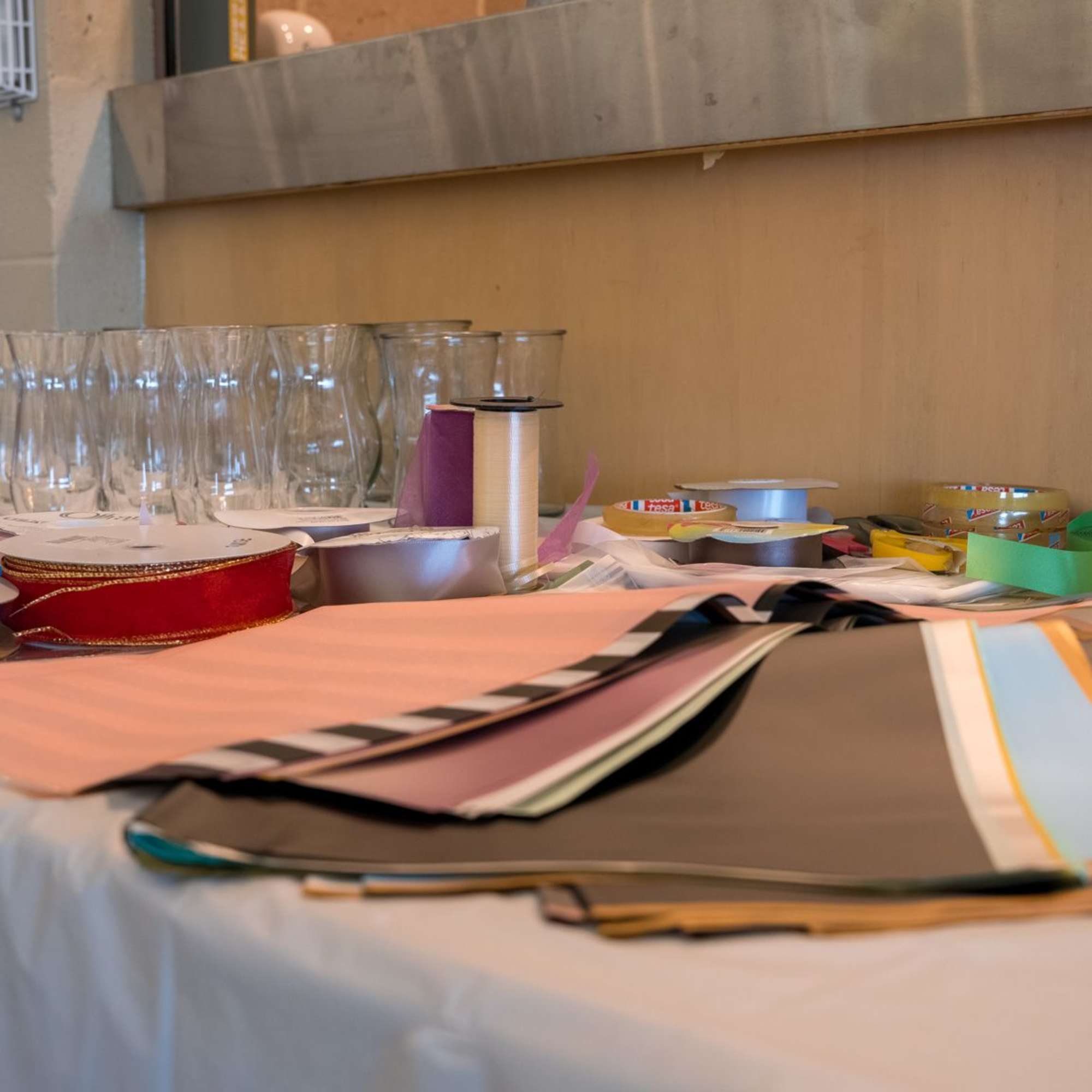 Table with ribbons, paper sheets, and glass vases arranged for crafting