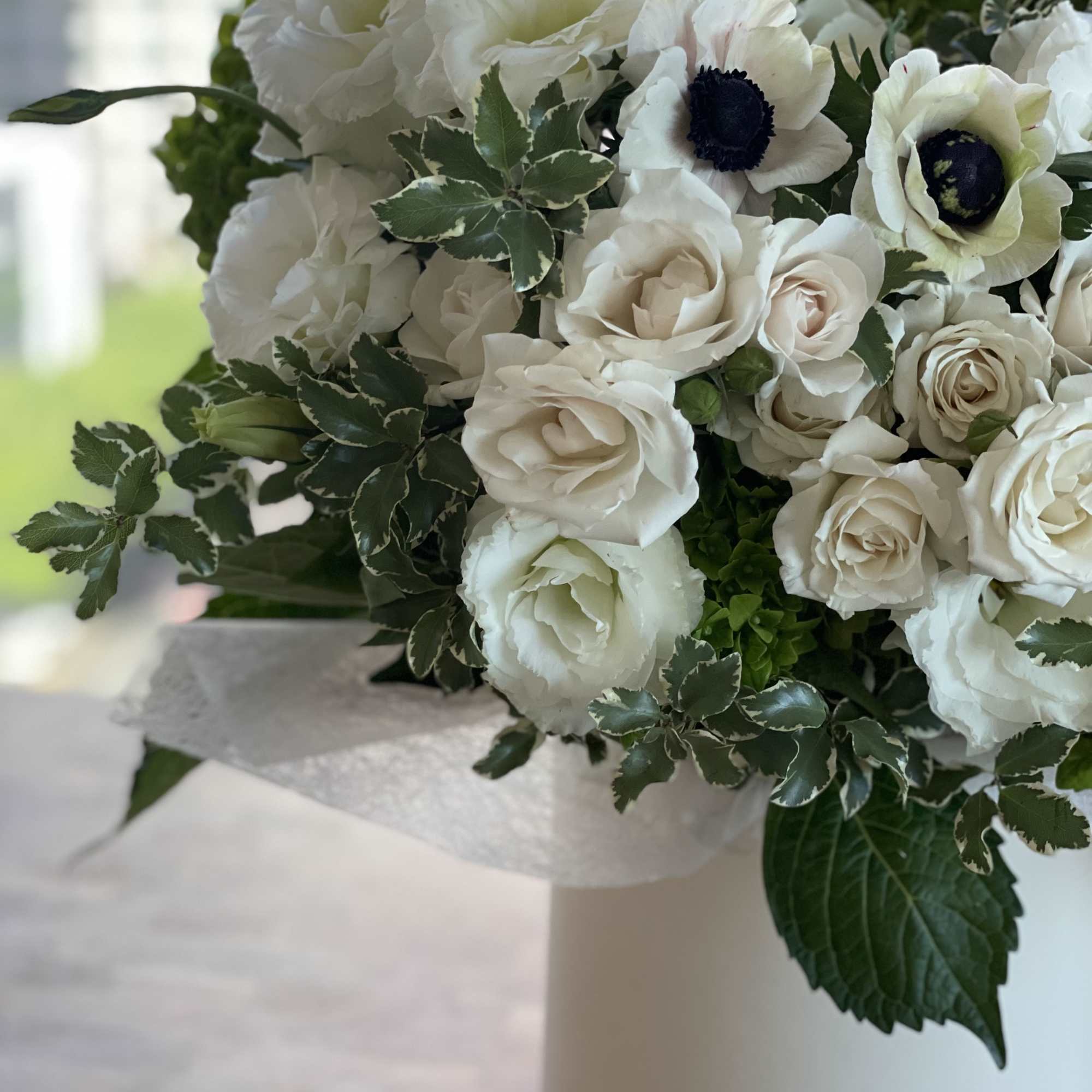 White roses, lisianthus, and anemone-style blooms arranged in a white cylinder box