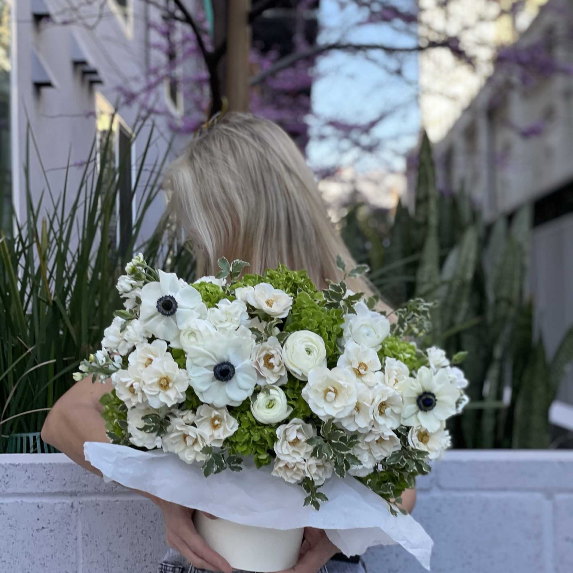 Large white and green flower arrangement in a low white vase held by a person outdoors