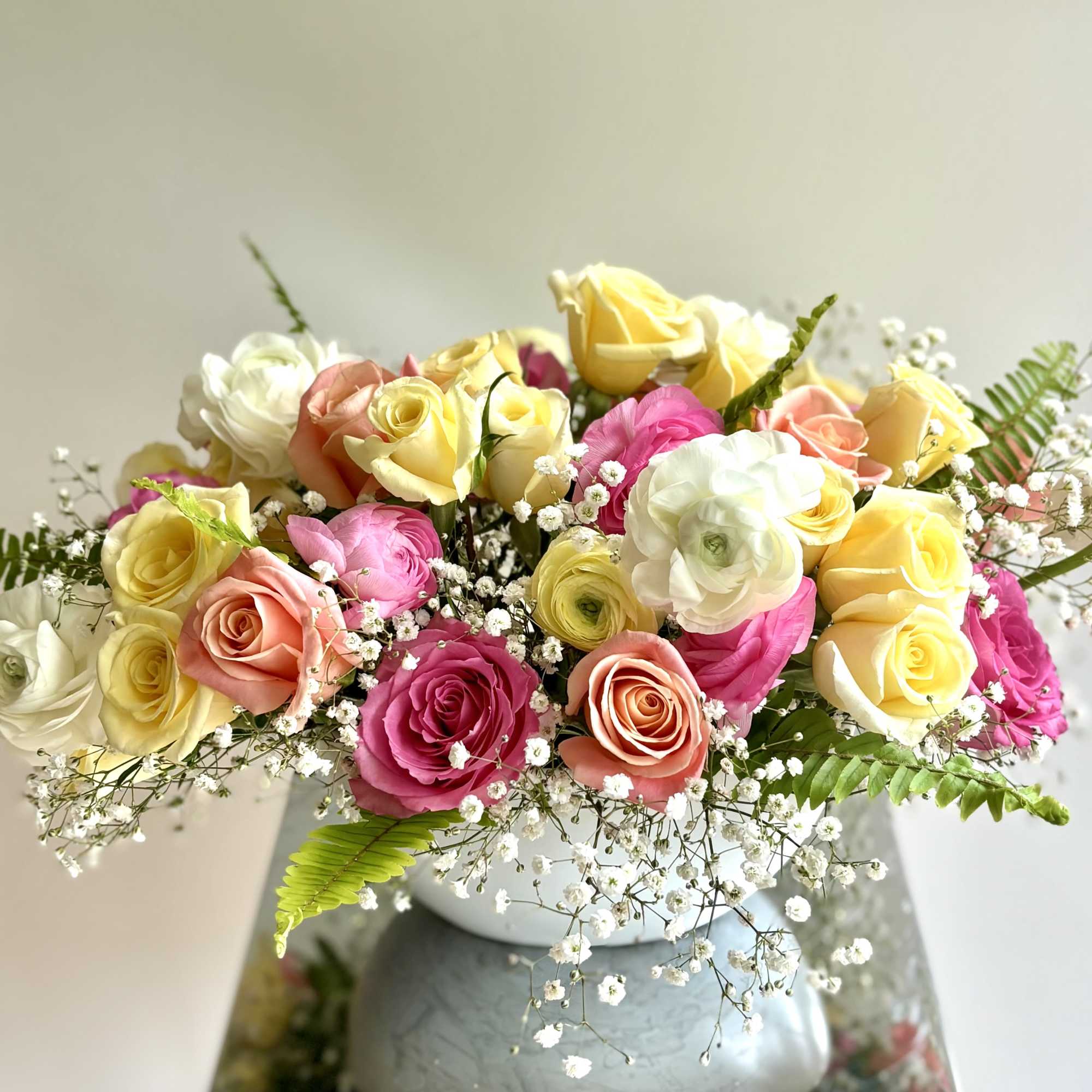 Mixed roses in pink, yellow, peach, and white arranged in a white vase