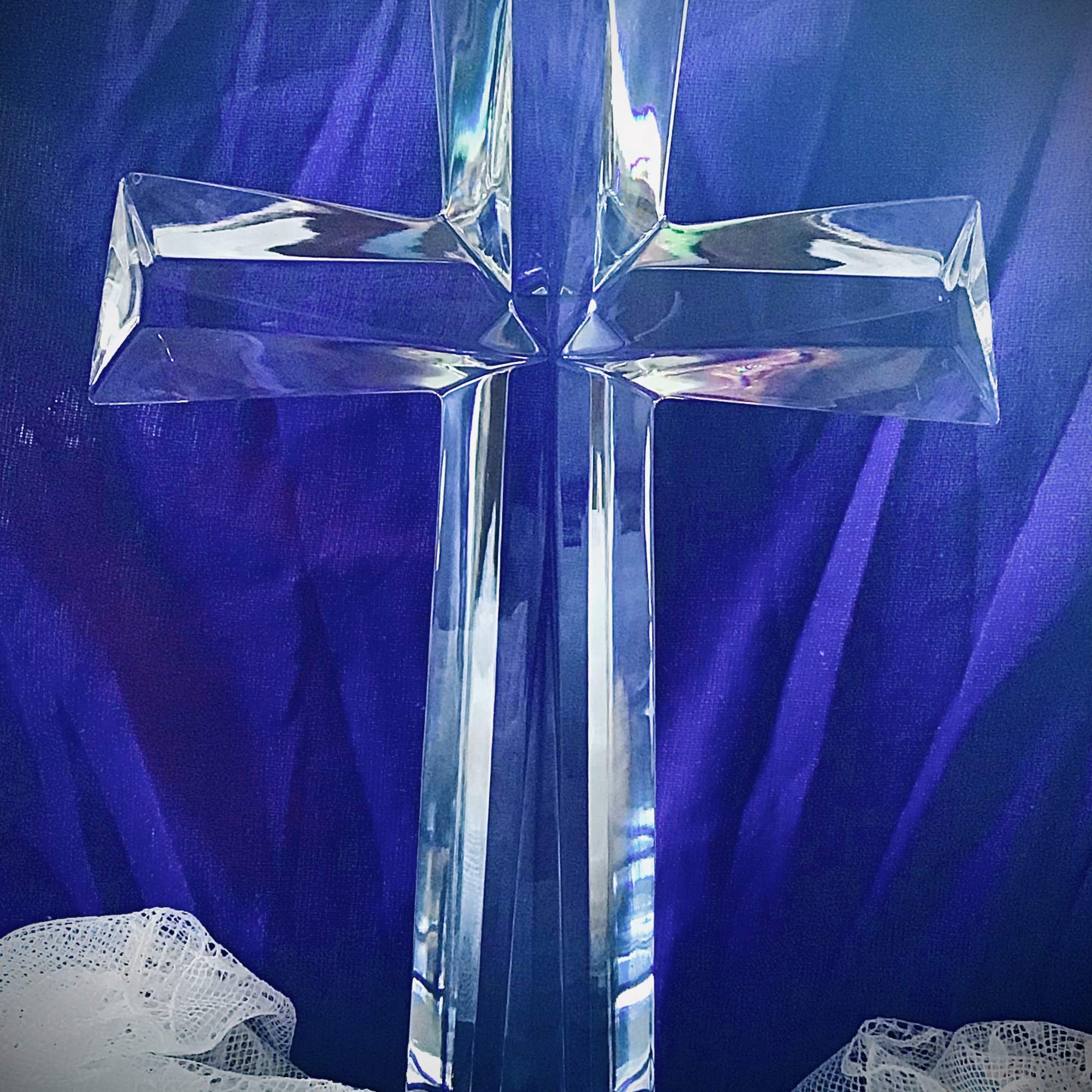 Clear glass cross on a purple fabric background with white lace at the bottom