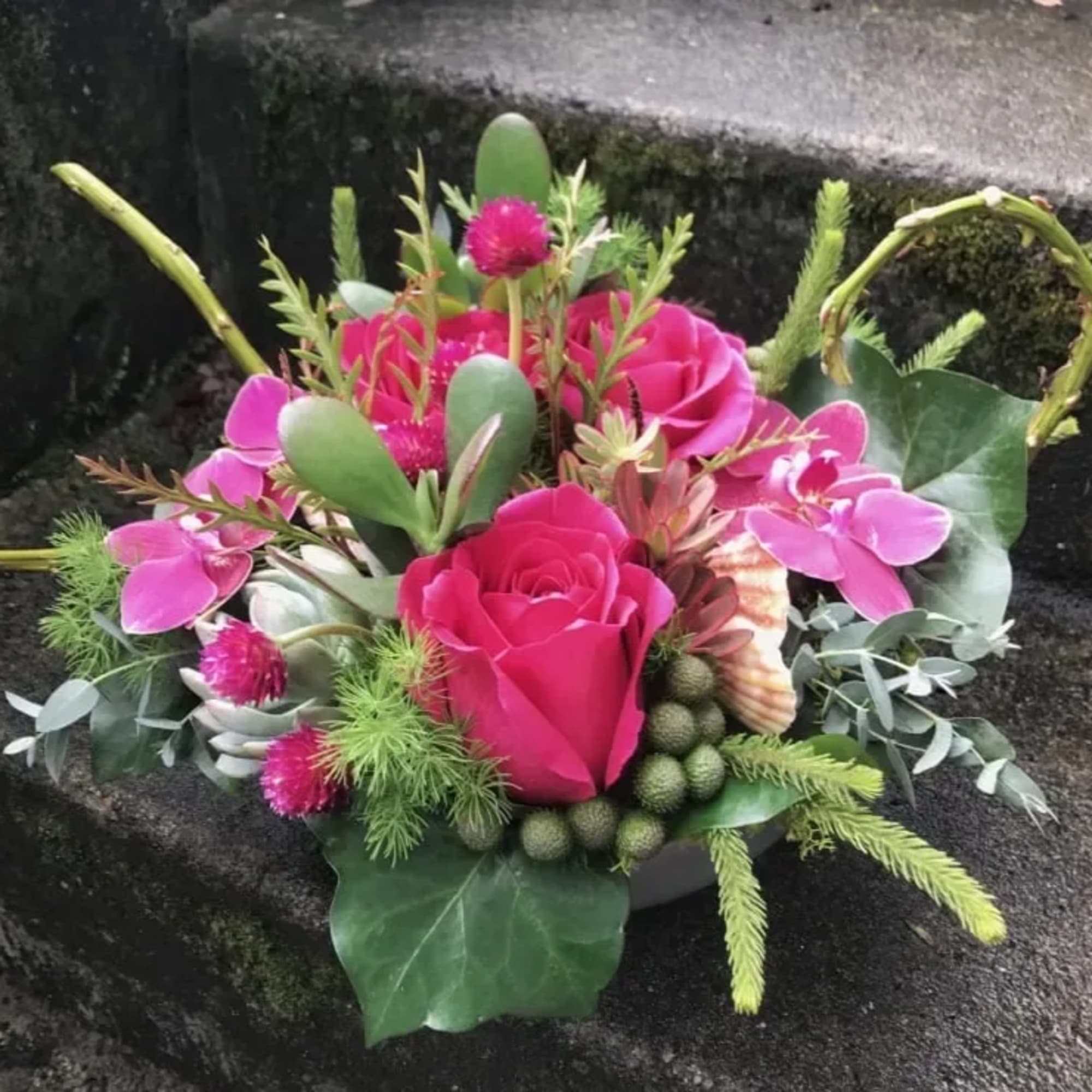 Pink roses and orchids arranged with succulents and greenery in a basket