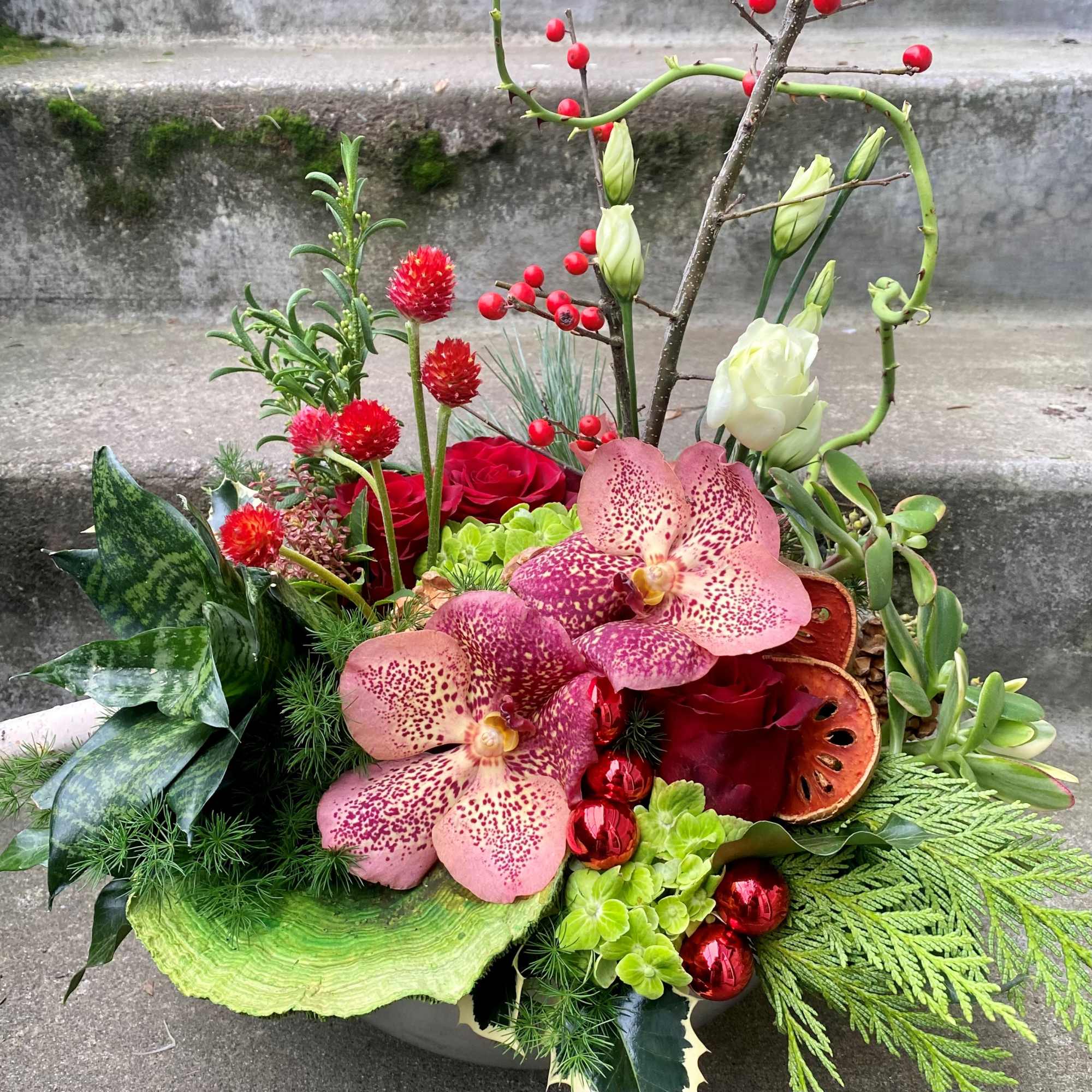 Mixed floral arrangement with pink orchids, red roses, and berries in a low container