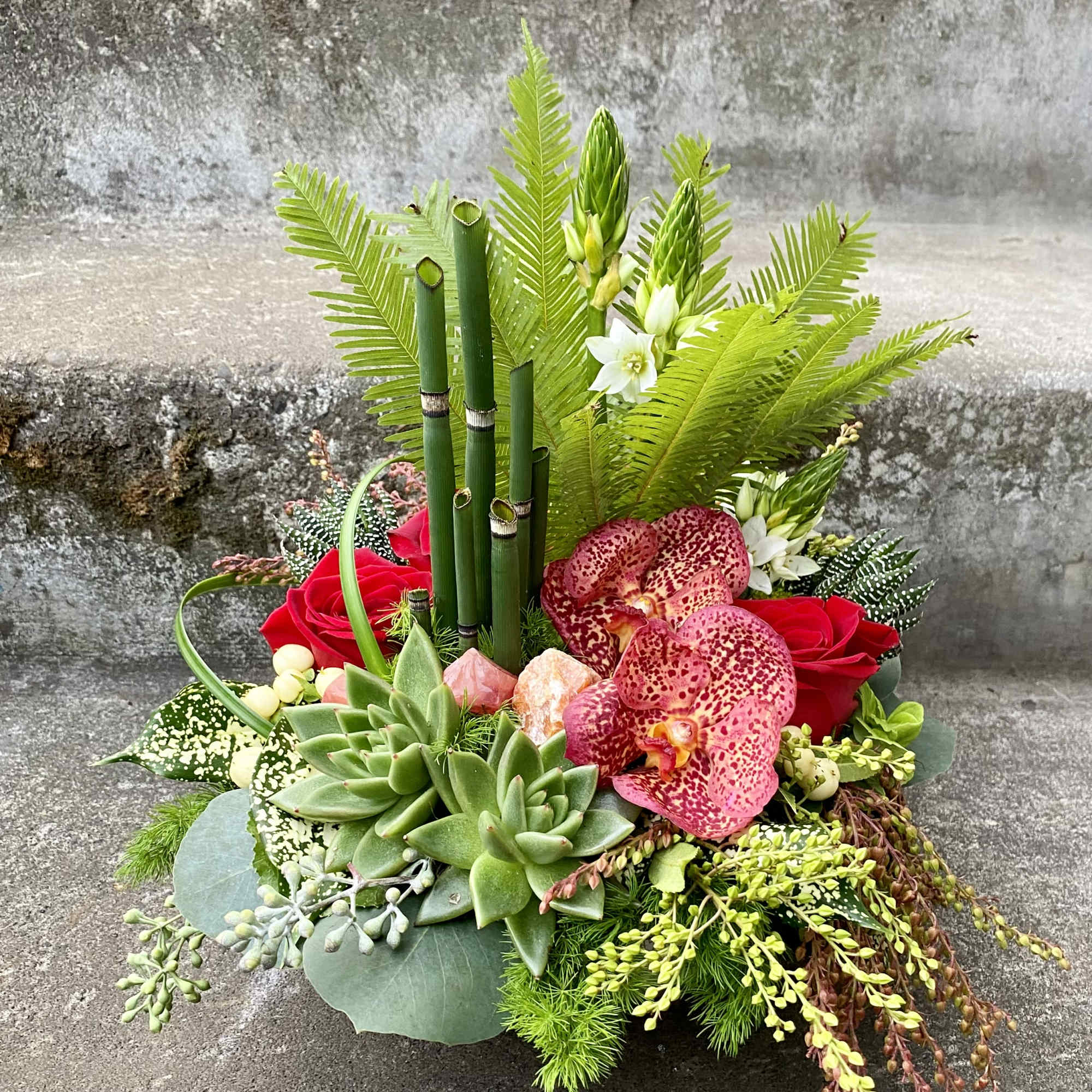 Tropical arrangement with red roses, orchids, and succulents