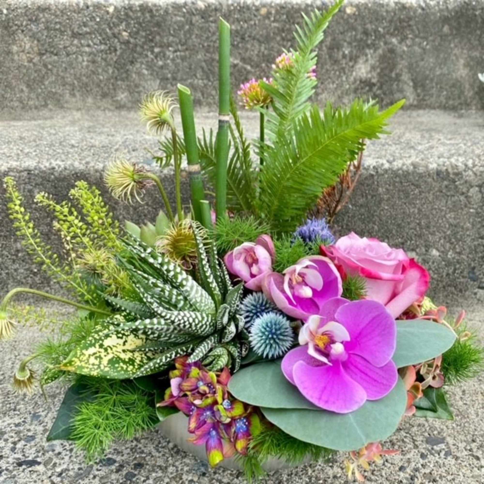 Tropical bouquet with pink roses and purple orchids in a low container