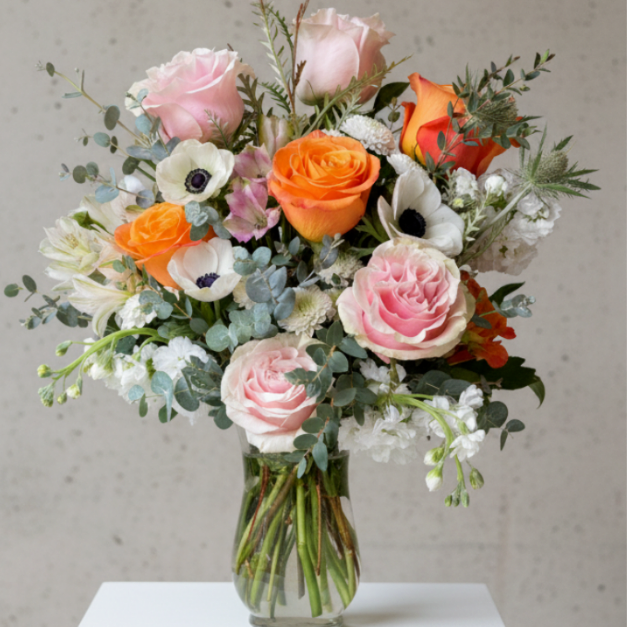 Mixed bouquet of pink and orange roses with white anemones in a clear glass vase