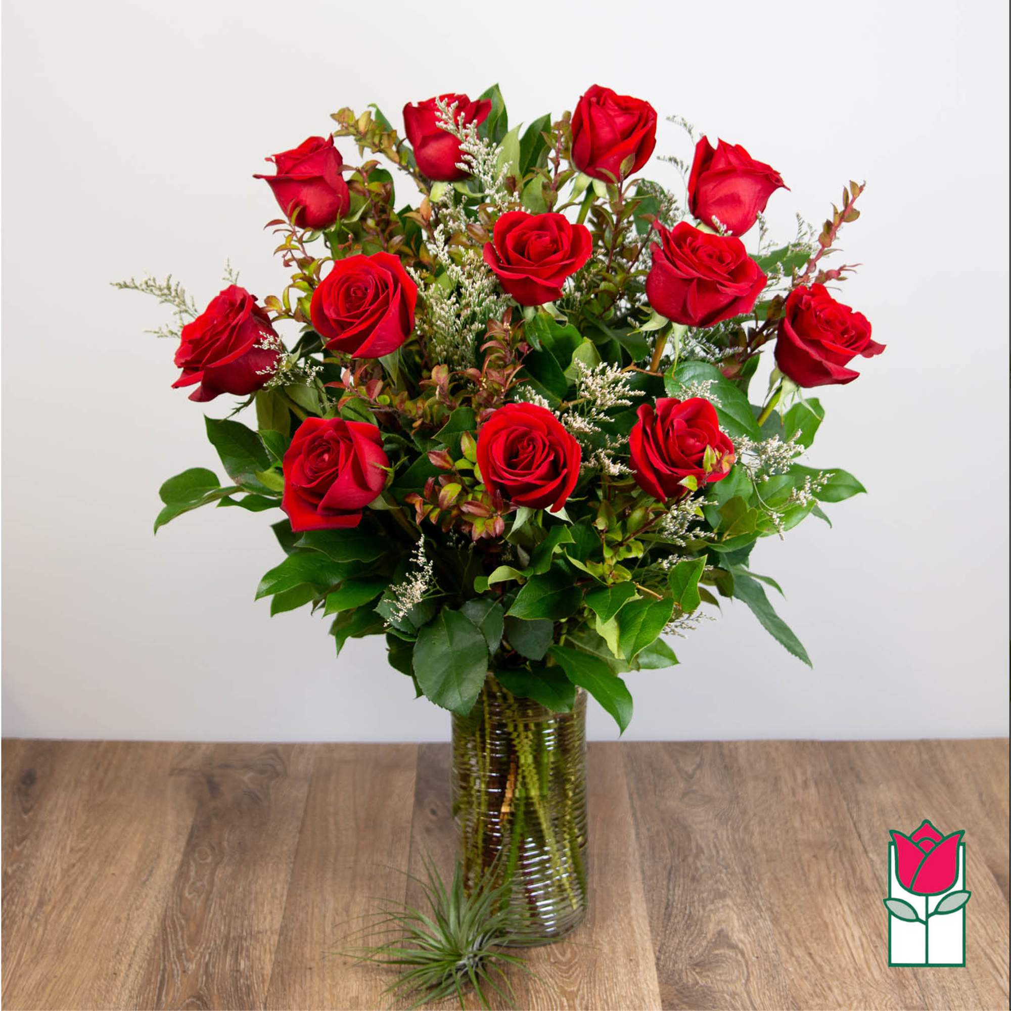 Red roses arranged in a clear glass vase with greenery