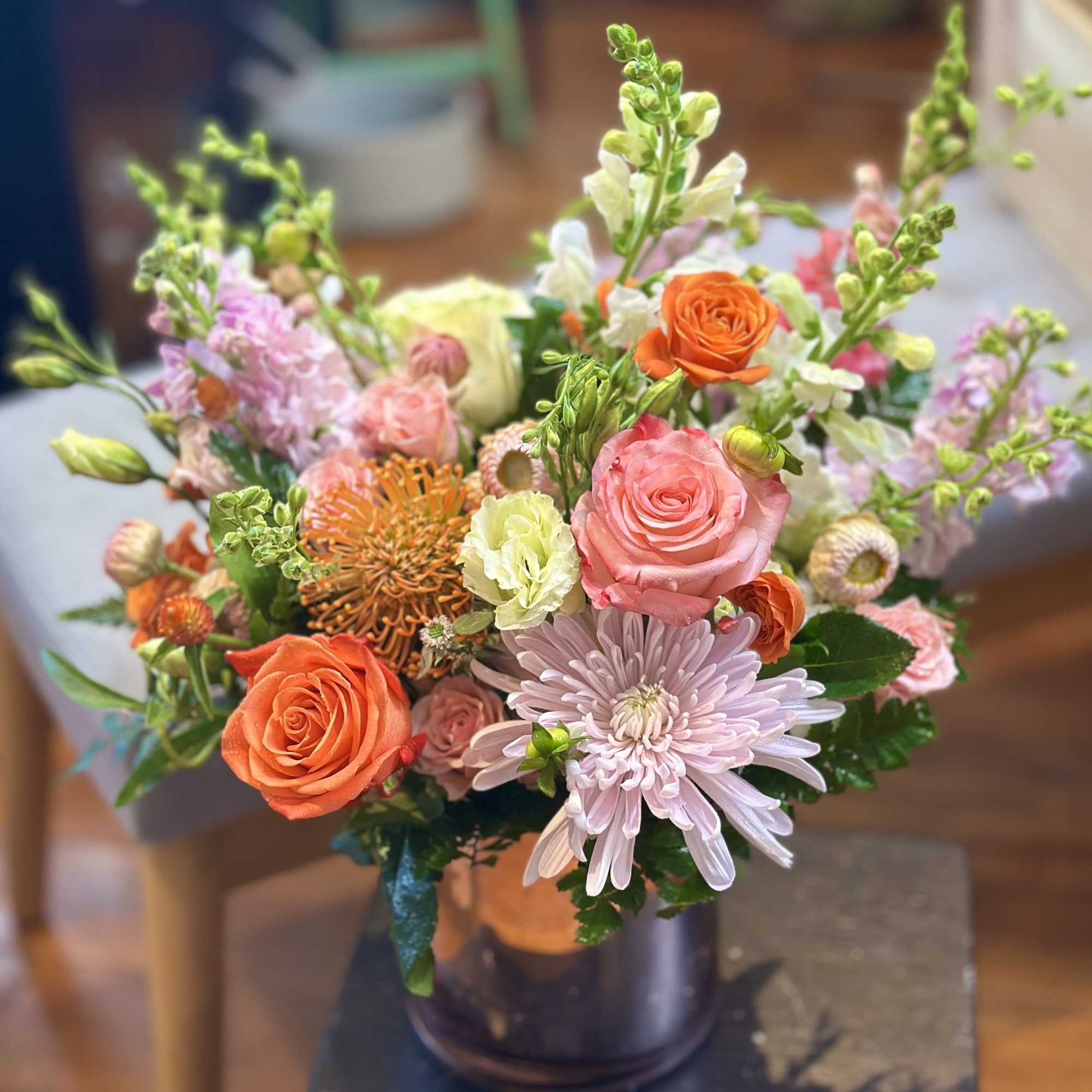 Mixed arrangement of pink and orange roses, mums, and snapdragons in a metallic vase