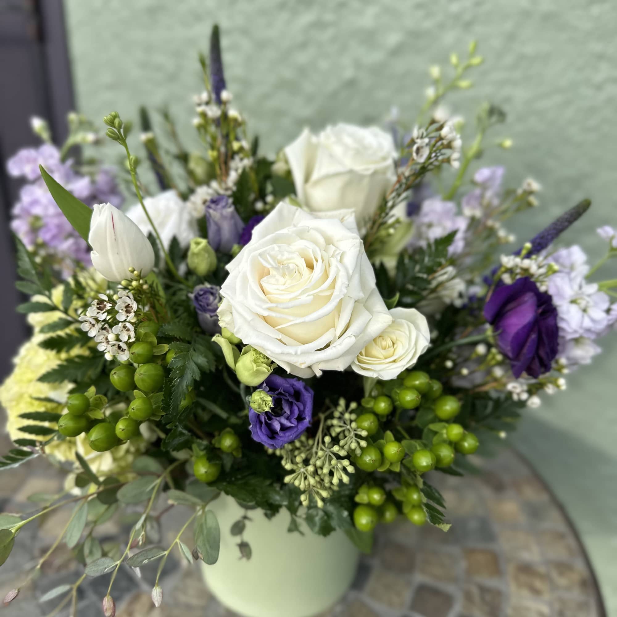 Arrangement of white roses and purple flowers in a light green vase on a mosaic table