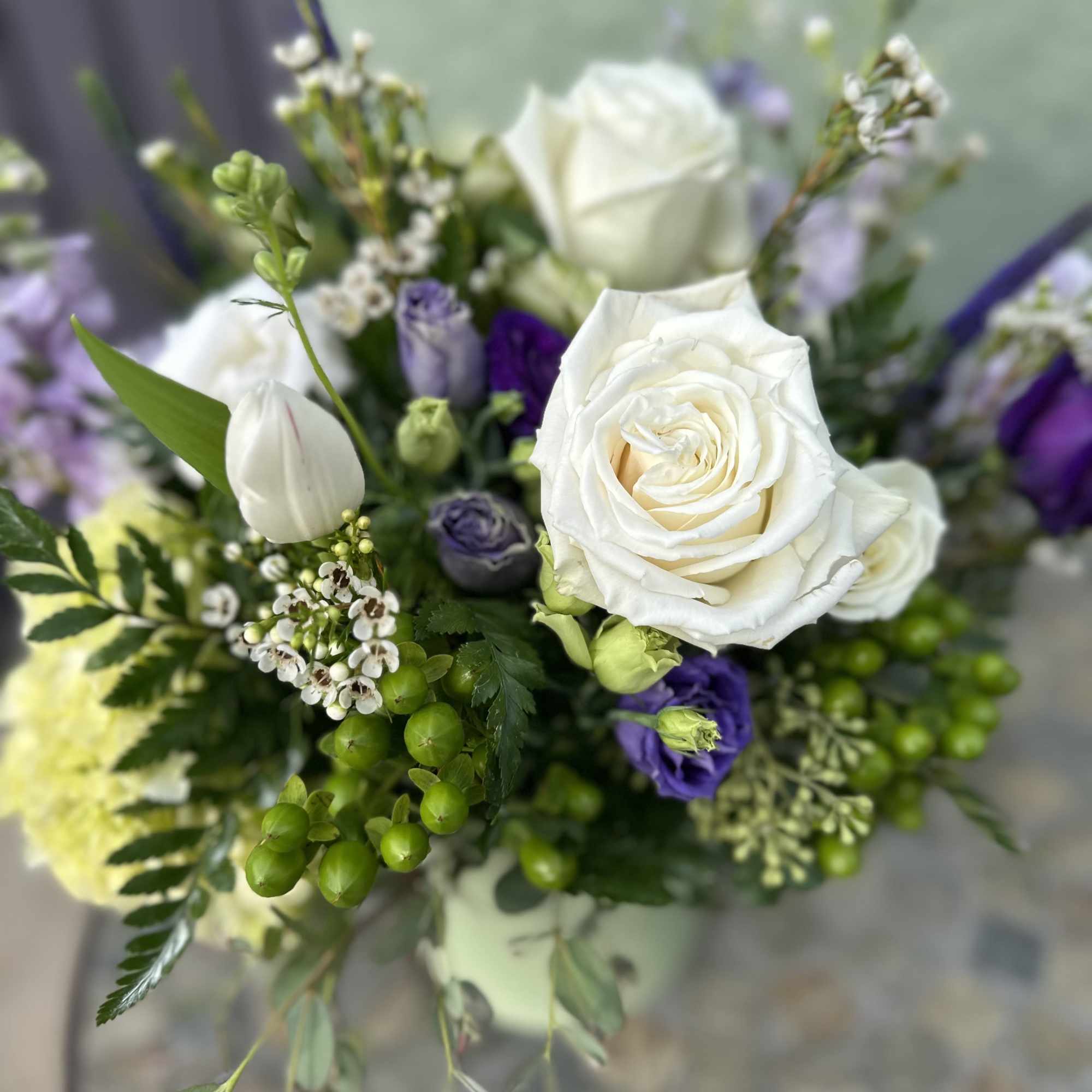 Medium vase arrangement with white roses, purple blooms, and green berries.