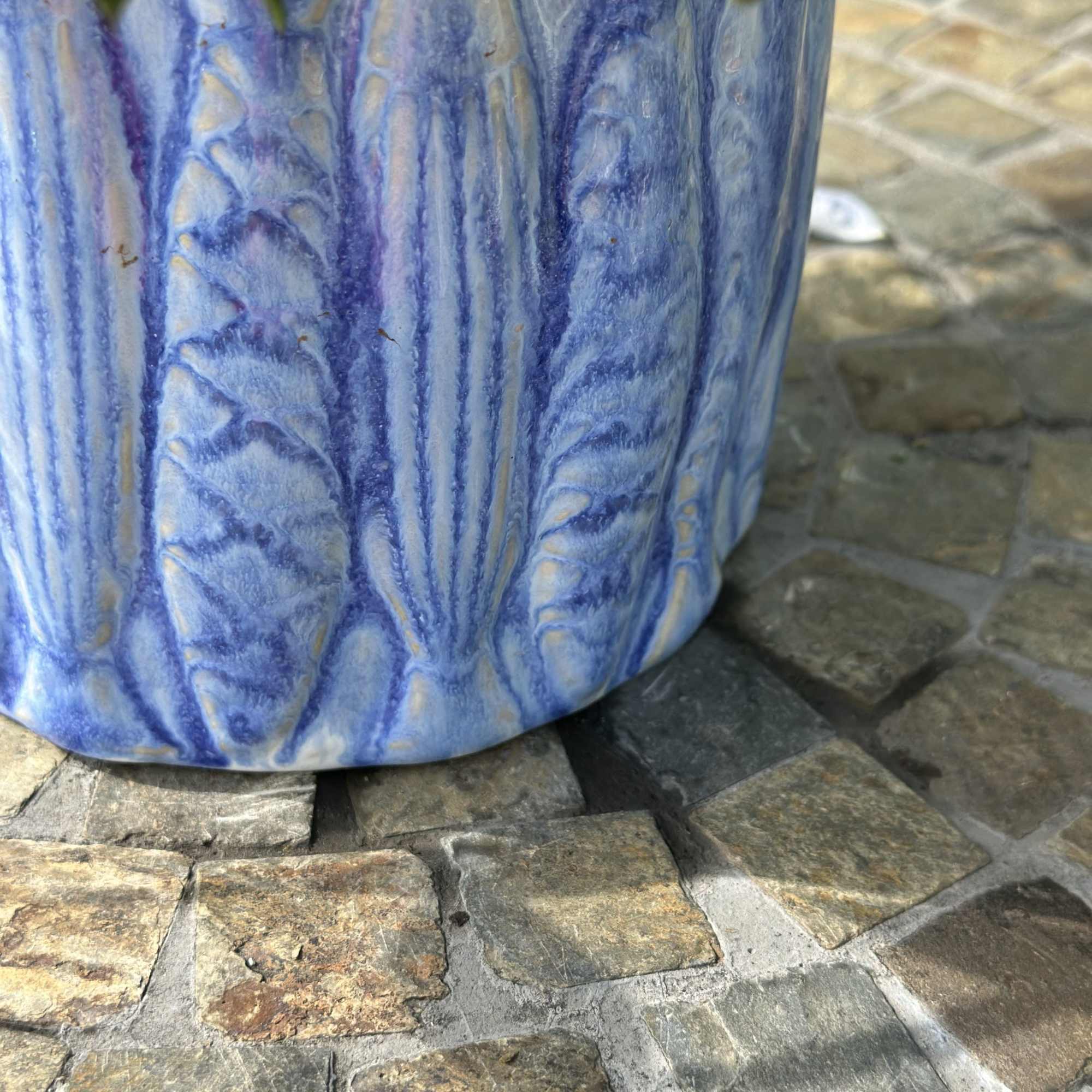 Textured blue ceramic planter with a plant, sitting on a stone tile surface