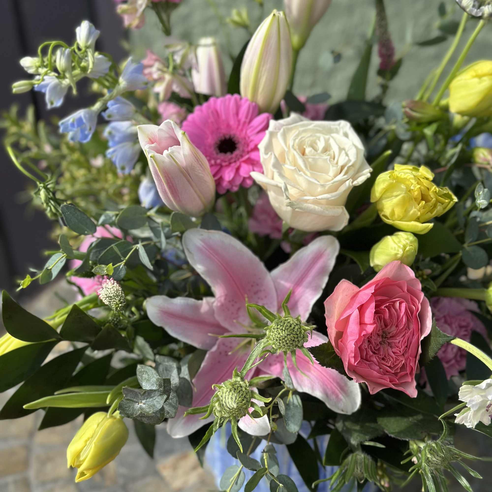 Mixed bouquet of pink lilies, roses, gerbera daisies and yellow tulips in a blue ceramic vase