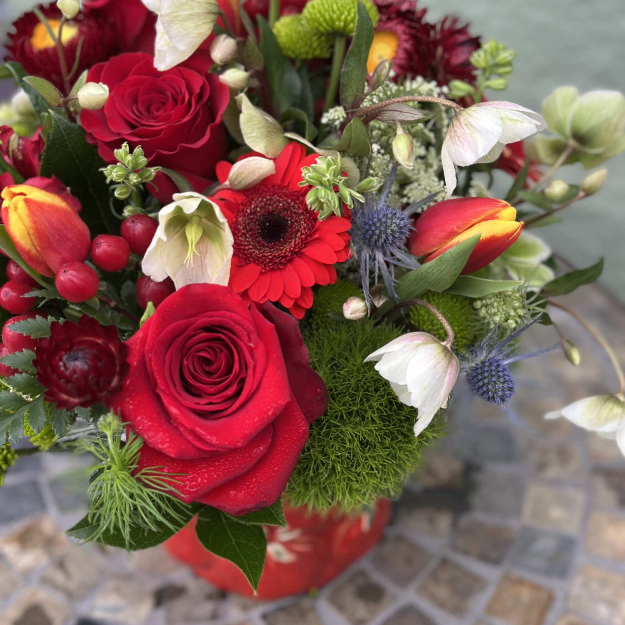 Vibrant arrangement of red roses, gerbera daisy, tulips and mixed blooms in a red ceramic container
