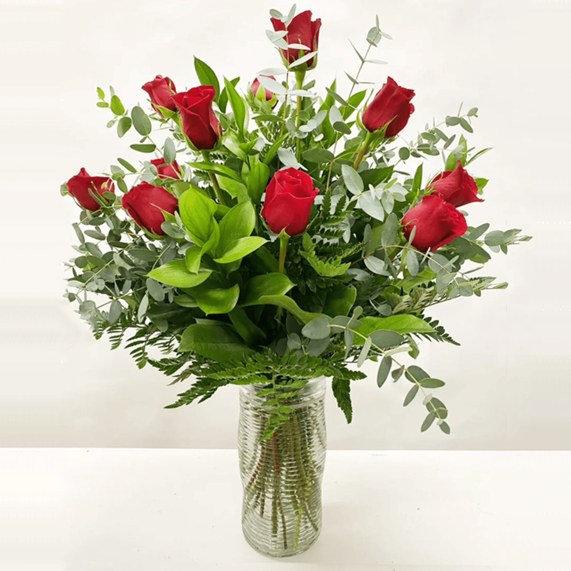 Tall arrangement of red roses and abundant greenery in a clear glass vase