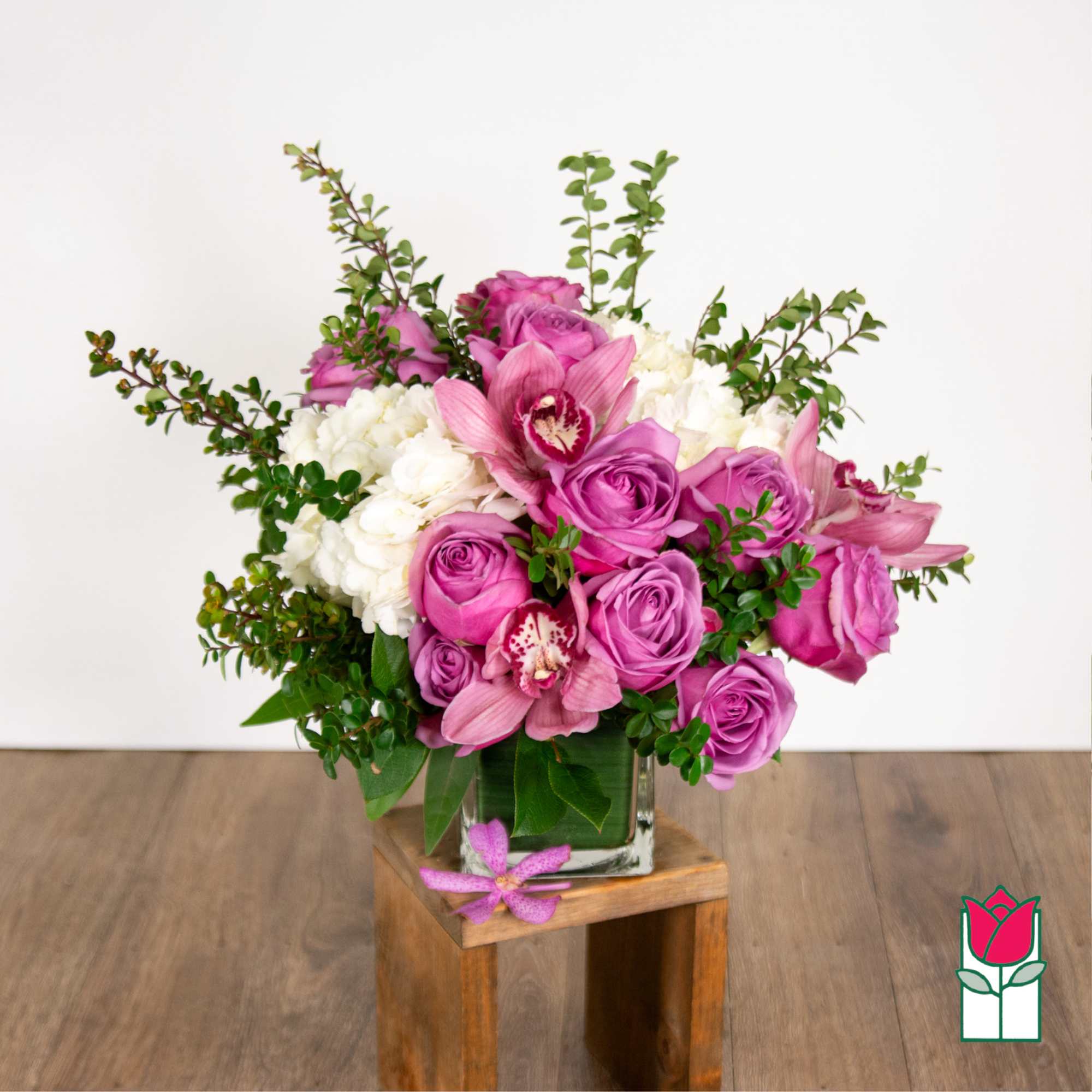 Pink roses and orchids arranged in a square glass vase