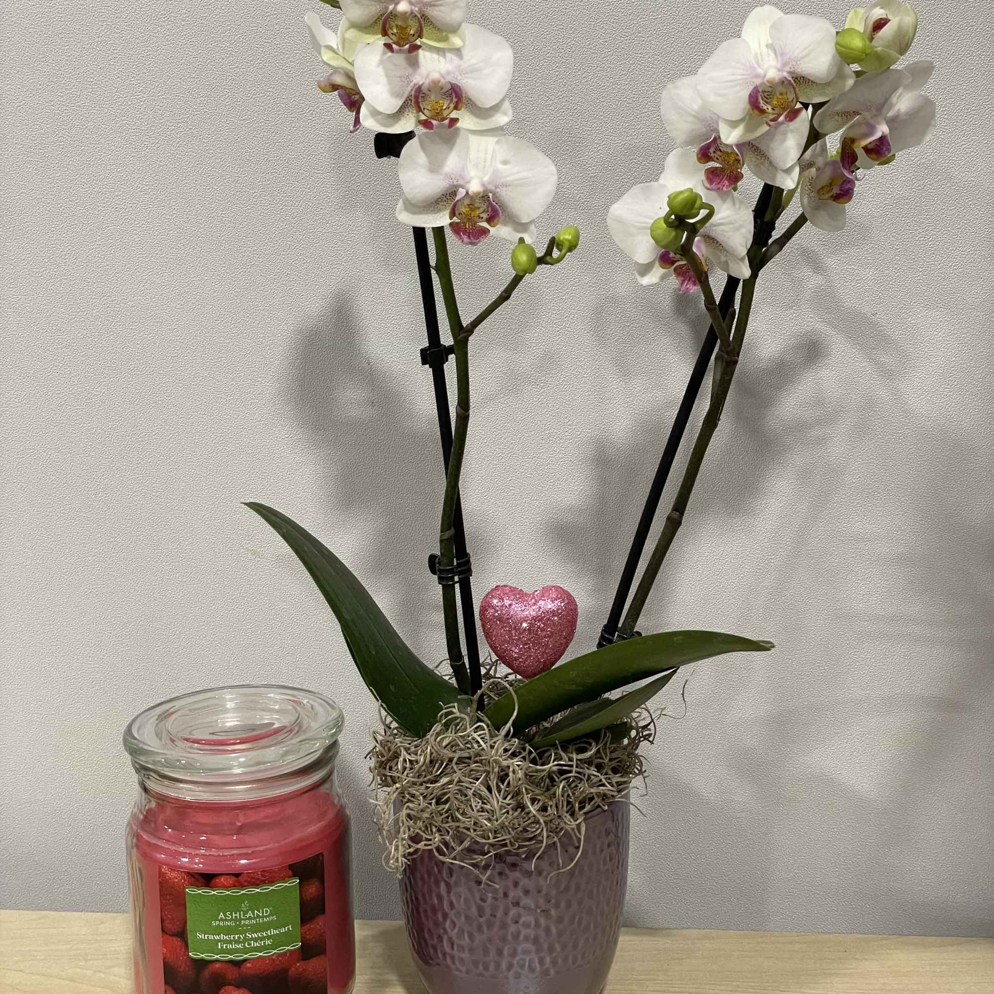 White orchids in a purple pot beside a pink candle jar