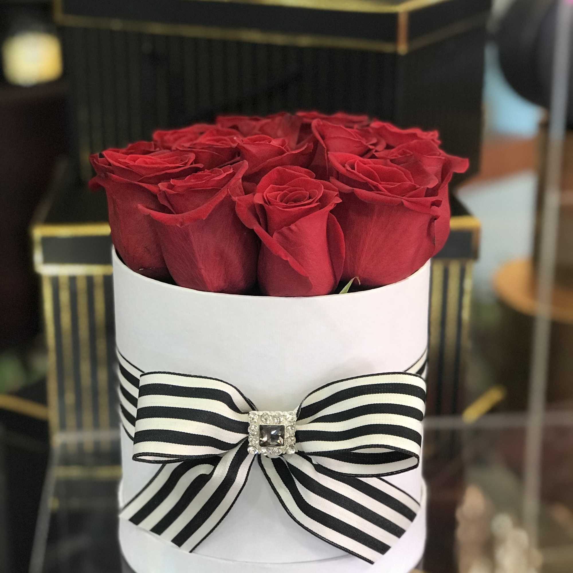 Red roses arranged in a white round box with a striped bow