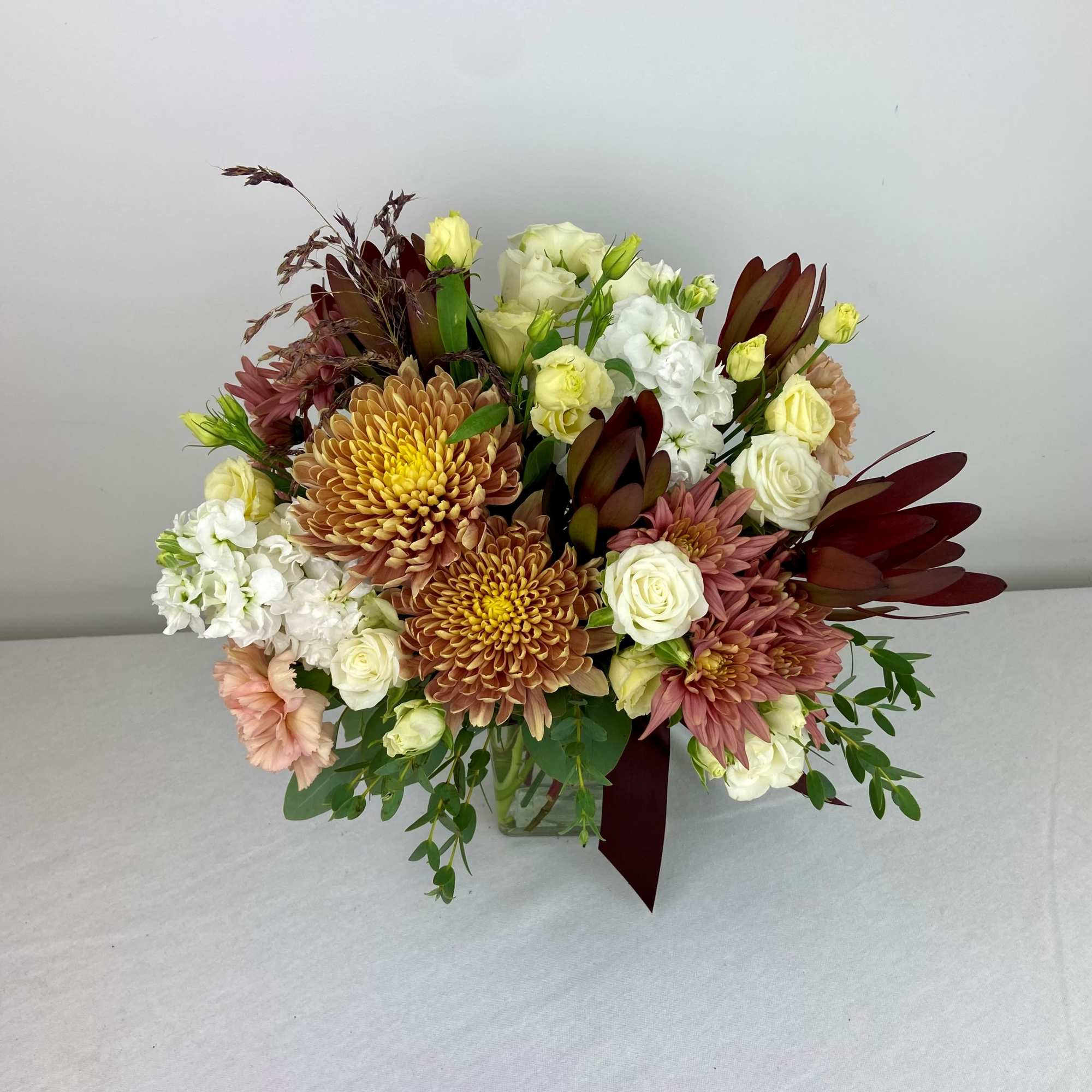 Mixed bouquet of chrysanthemums, white roses, and pale blooms in a glass vase