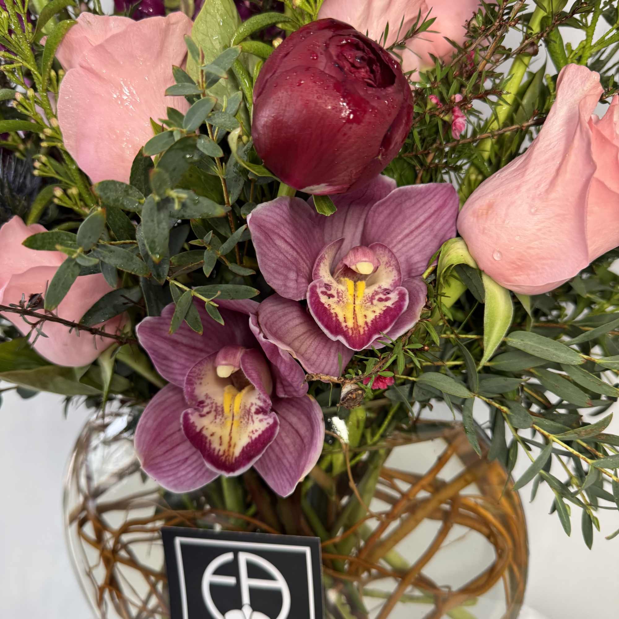 Pink and purple bouquet with orchids and a dark red bloom in a glass vase