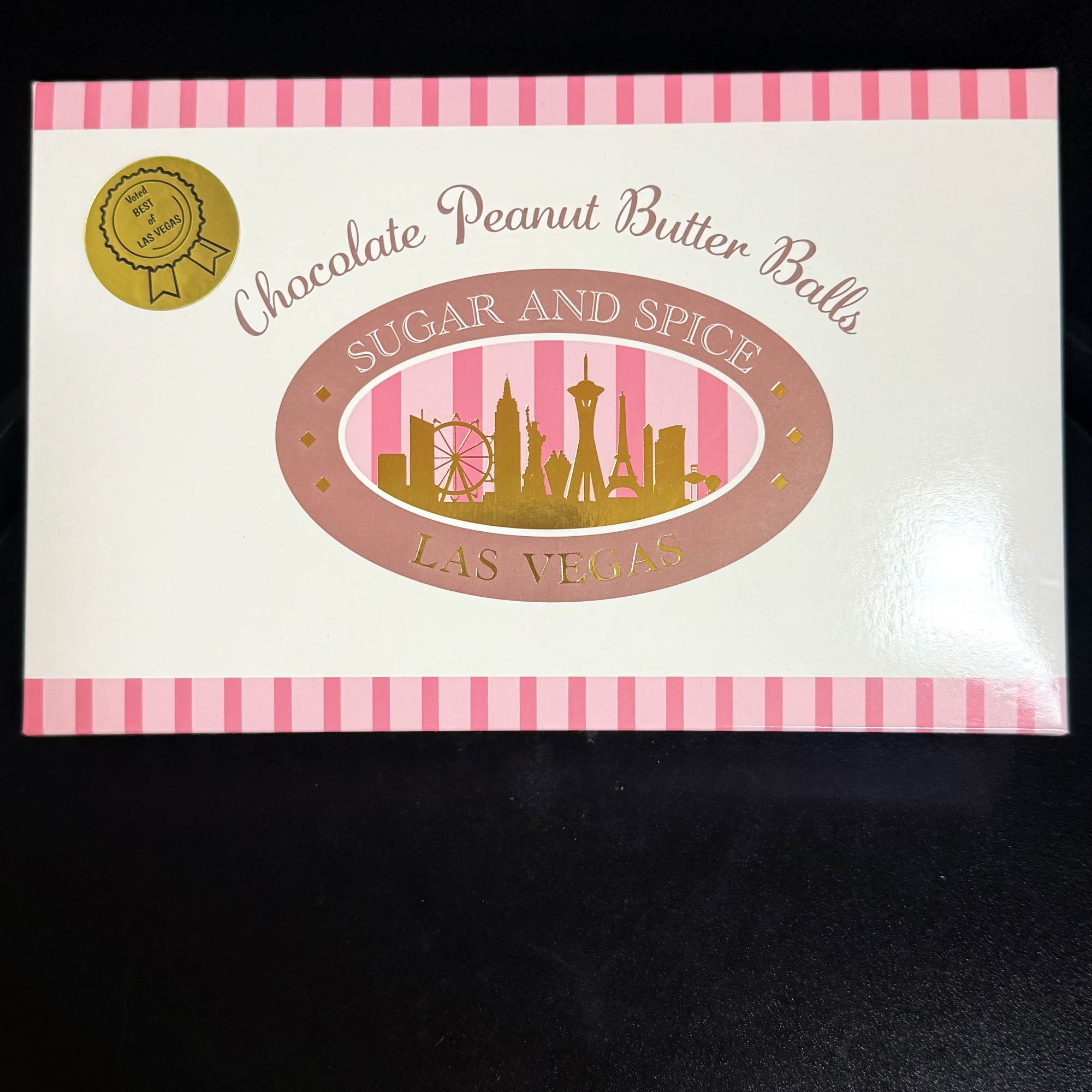 Rectangular box of Sugar and Spice Las Vegas chocolate peanut butter balls with pink stripes on white.