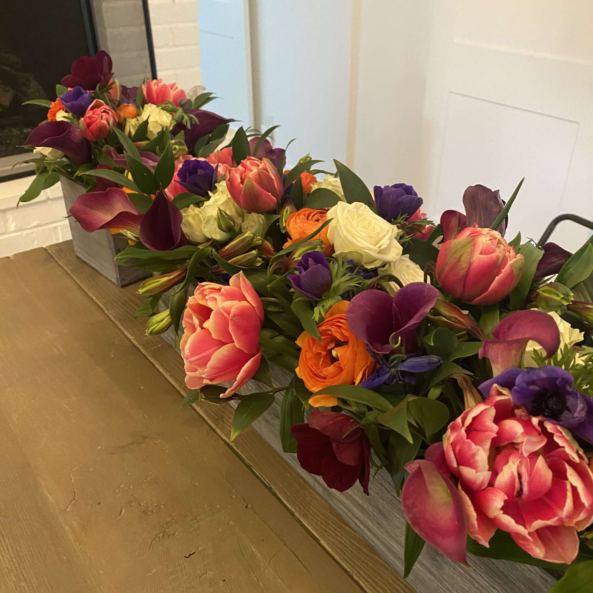 Long low floral arrangement with tulips, roses, calla lilies, and purple blooms